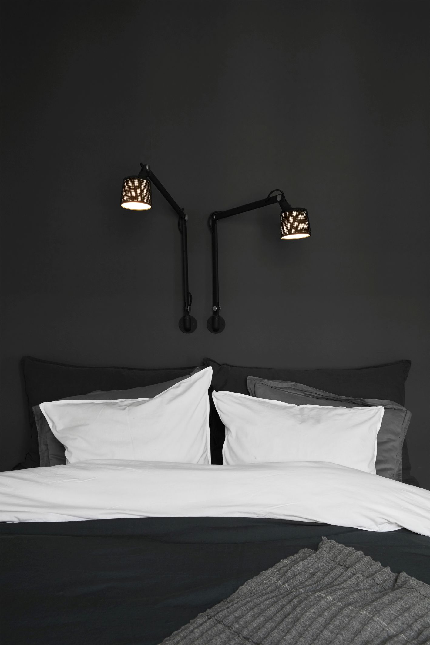 Schlafzimmer mit Bett und zwei schwarzen Vipp Wandlampen als Nachttischlampen an der dunklen Wand.