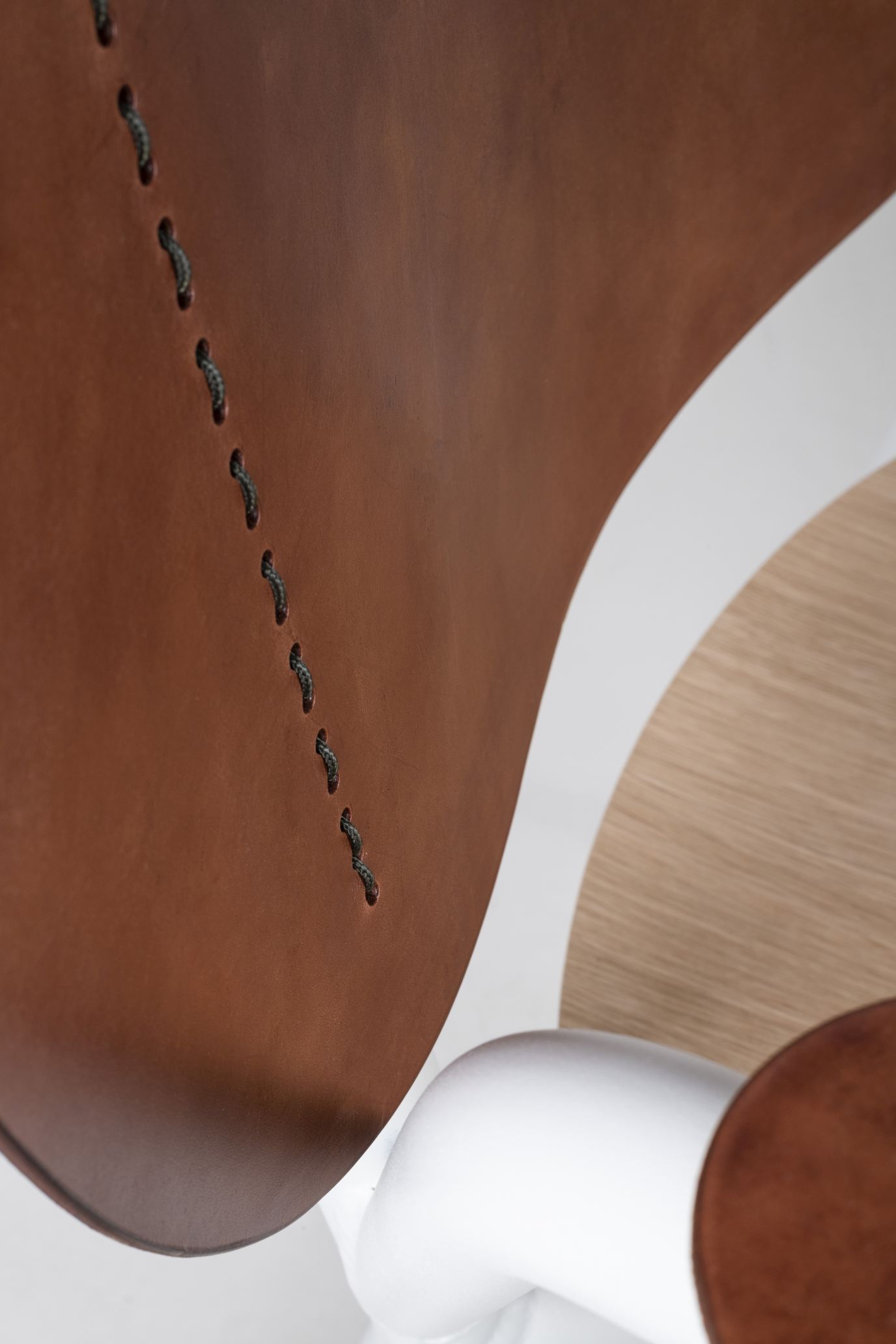 Detailaufnahme: Emil Rosi Armchair Stuhl mit braunem Leder, weißen Armlehnen und markanten Ziernähten.