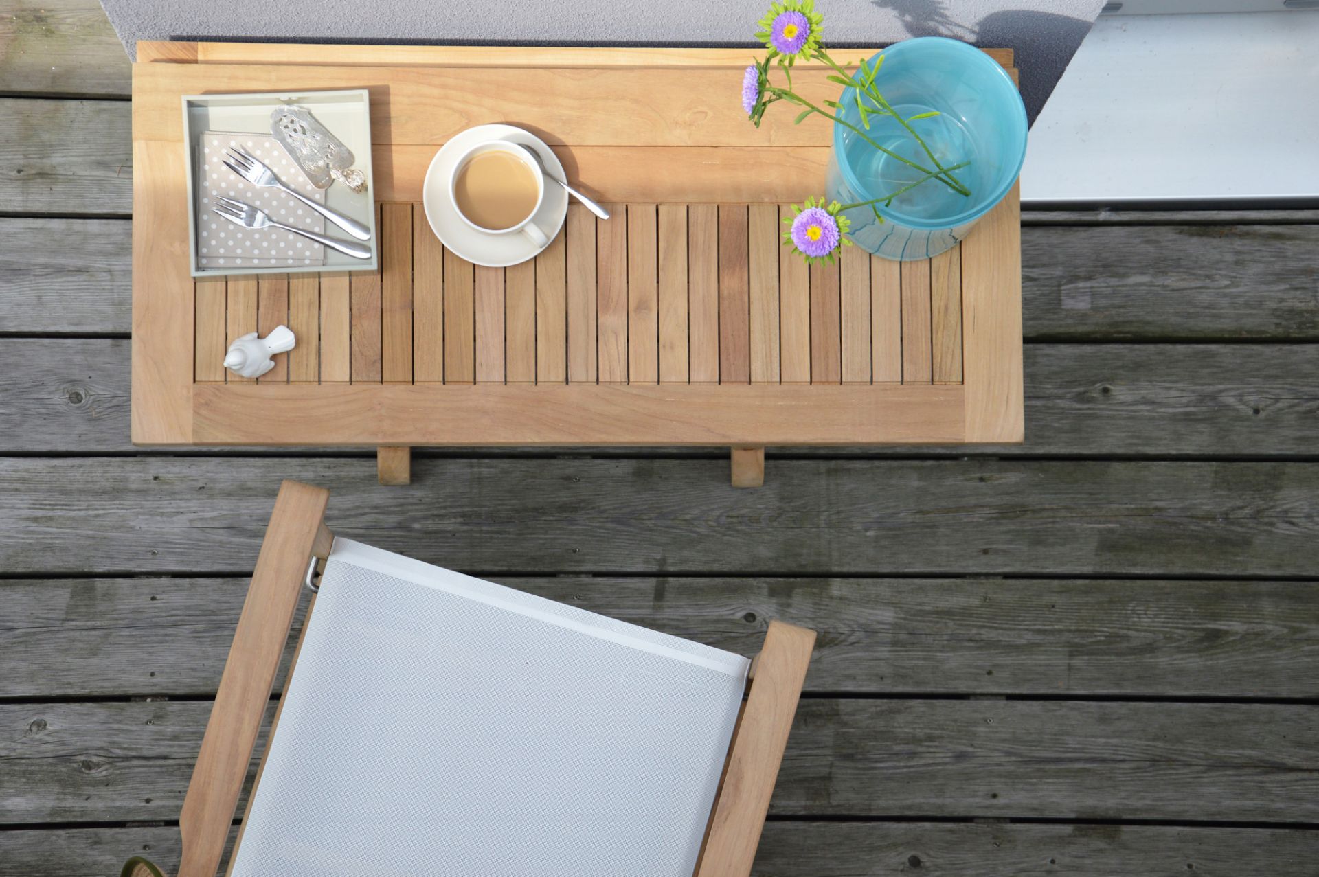 Teakholz Gartentisch mit Kaffeetasse, Blumen in Vase und Stuhl auf Holzterrasse von oben.