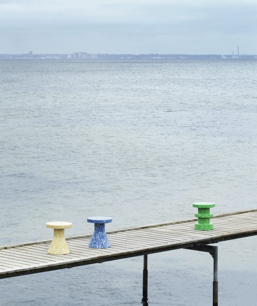 Drei bunte Bit Stool Cone Hocker von Normann Copenhagen auf einem Holzsteg am Meer.