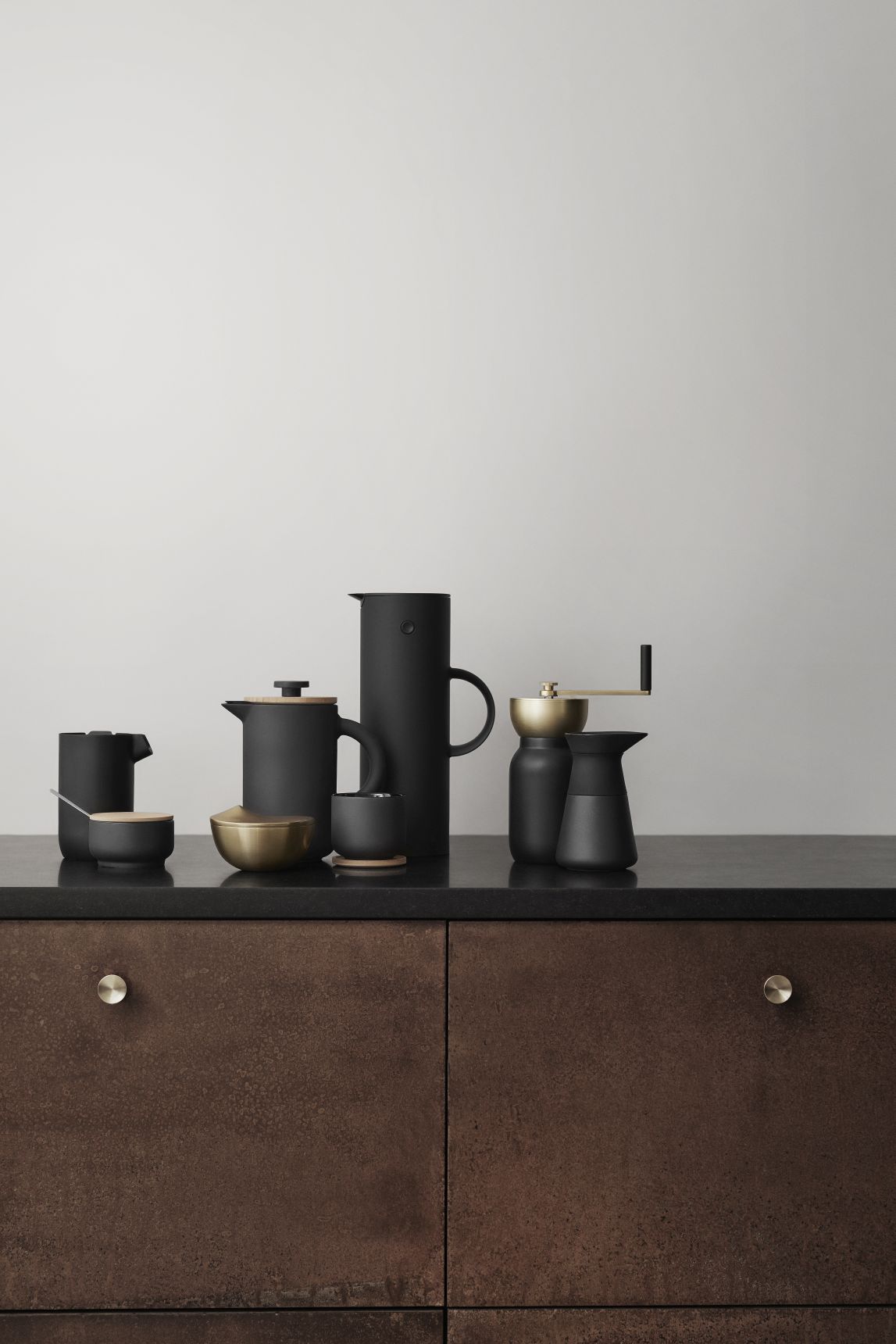 Produktfoto: Schwarzes Kaffeeset mit Kaffeemühle, French Press, Thermoskanne und Tassen auf dunkler Oberfläche.
