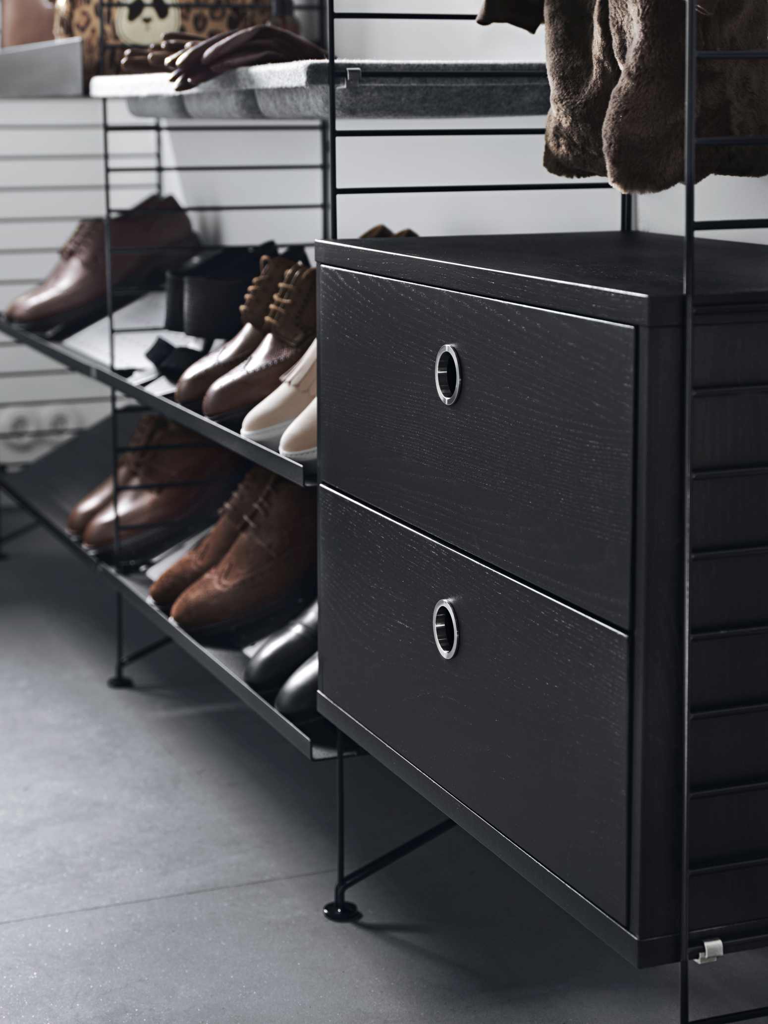 Schwarzer String Nachttisch mit zwei Schubladen und Schuhregalen im modernen Schlafzimmer.