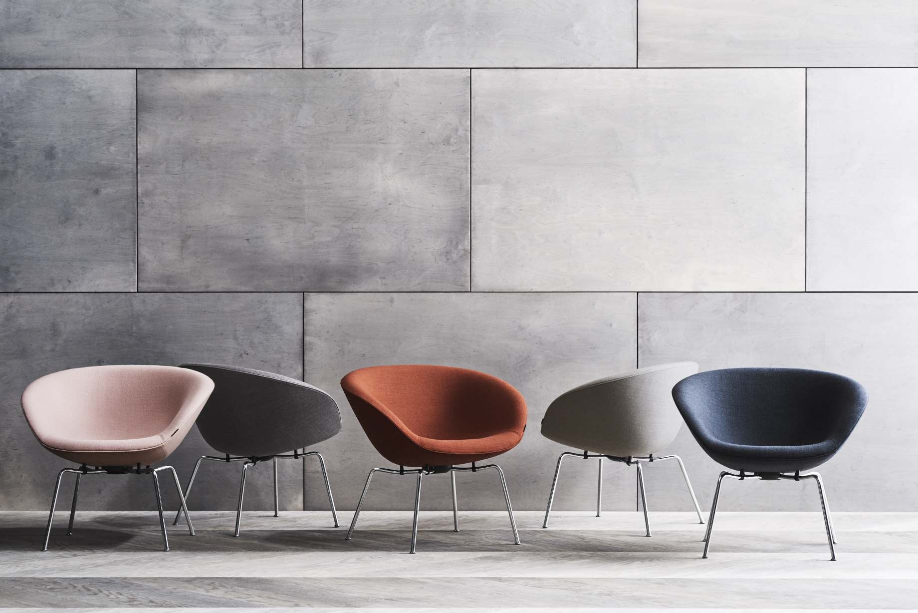 Fünf Fritz Hansen Pot Sessel in verschiedenen Farben vor einer grauen Wand.