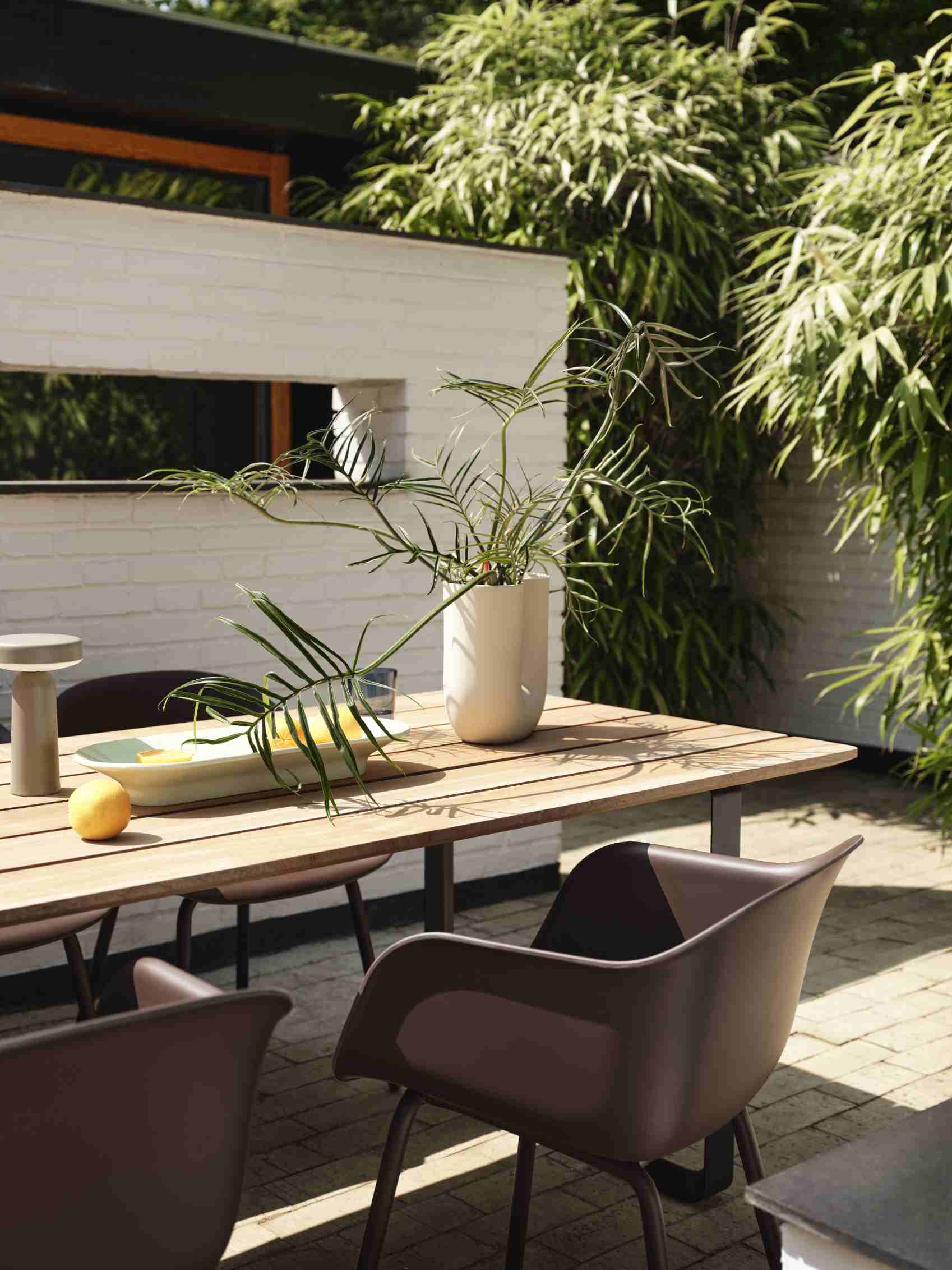 Muuto Fiber Outdoor Armchair: Brauner Armlehnstuhl aus Kunststoff am Holztisch im Garten.