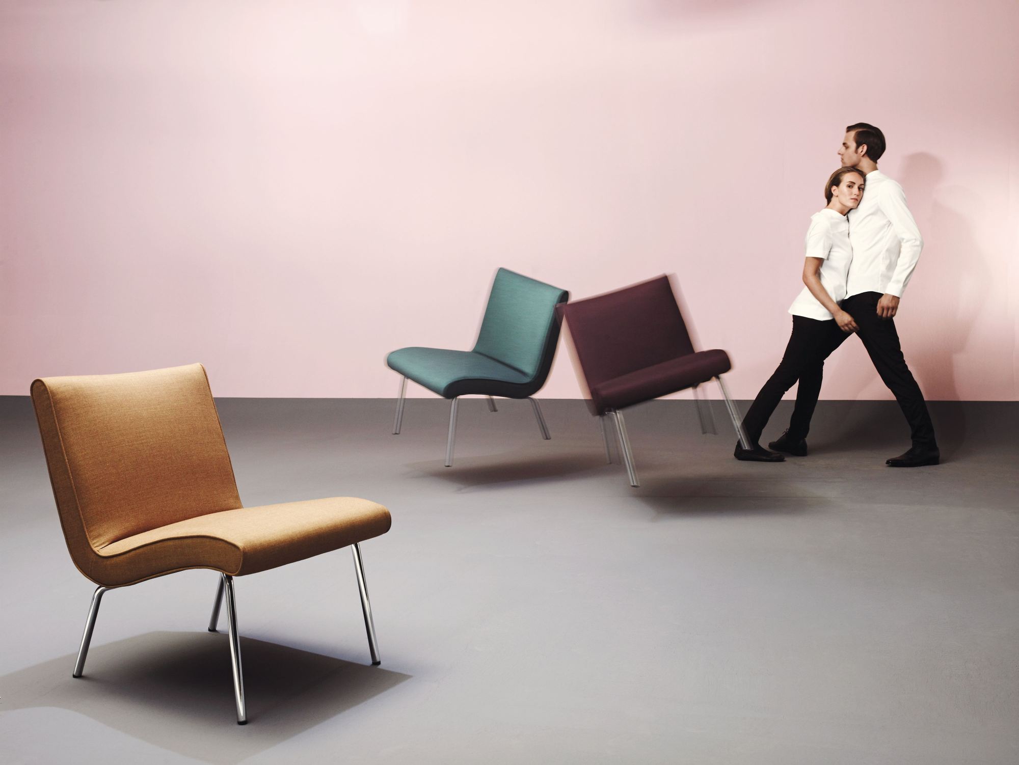 Walter Knoll Sessel 607 Vostra Armchair in Senfgelb, Türkis und Weinrot mit Paar im Hintergrund.
