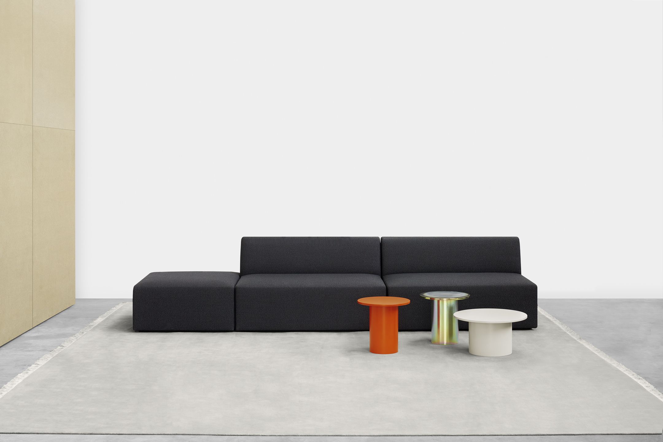 Enoki Beistelltische e15 in Orange, Gold und Weiß vor einem Sofa auf einem Teppich.