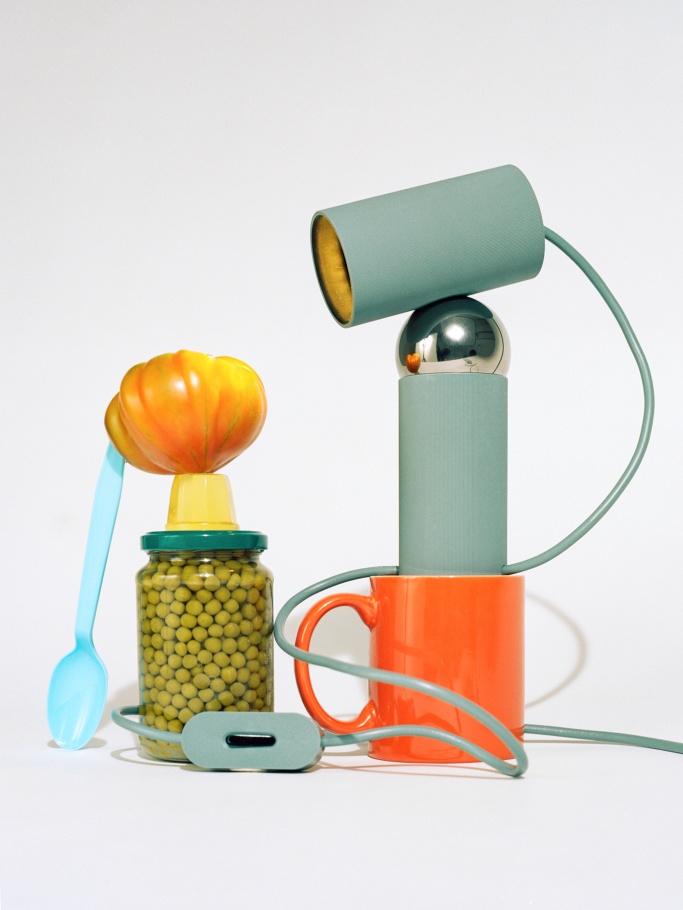 Verspielte Bilboquet Tischleuchte: Stillleben mit Lampe, Konservenglas, Tasse und Löffel vor weißem Hintergrund.