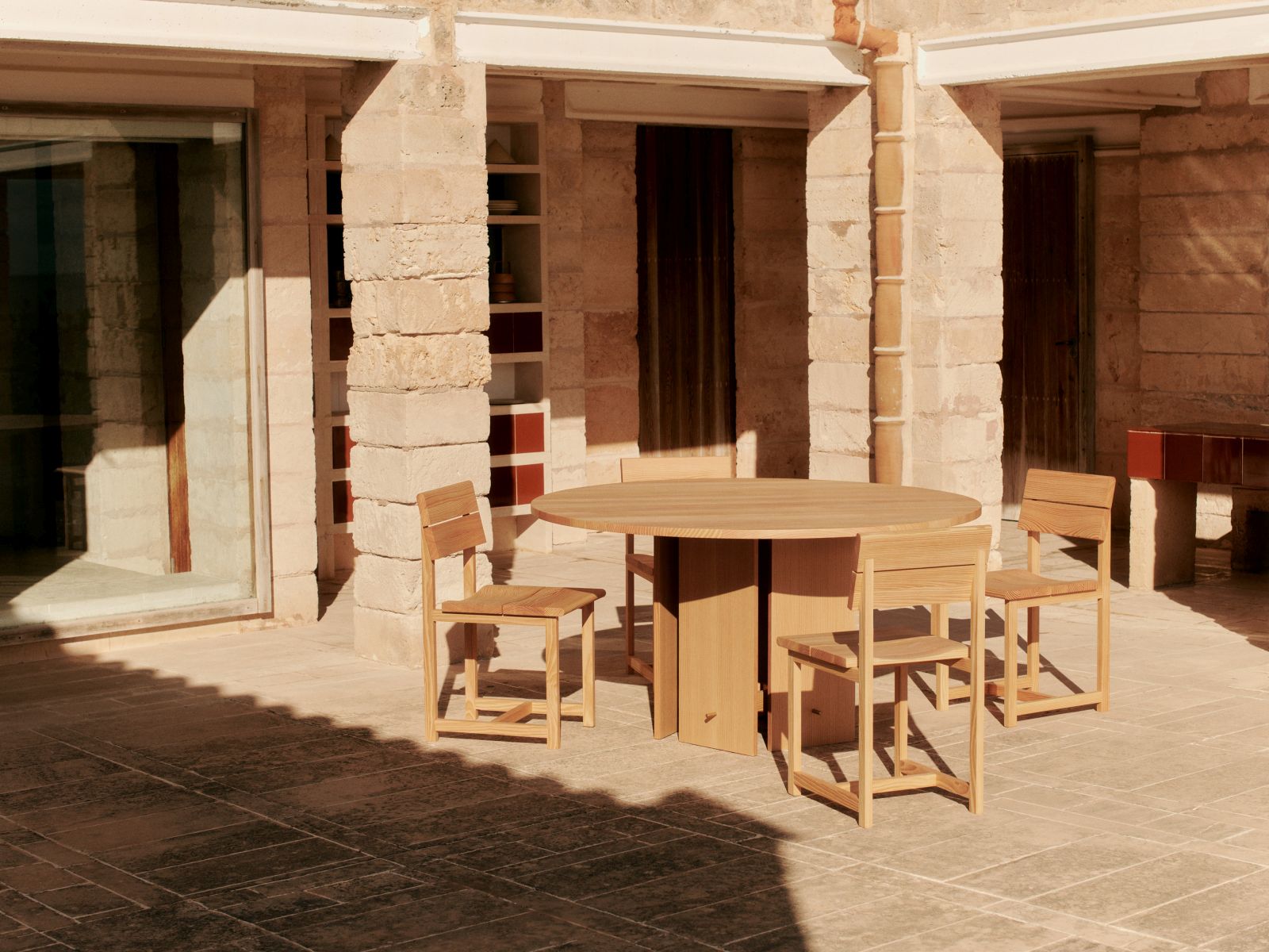 Ferm Living Visit Esszimmerstuhl aus Holz mit rundem Tisch und vier Stühlen im Außenbereich.