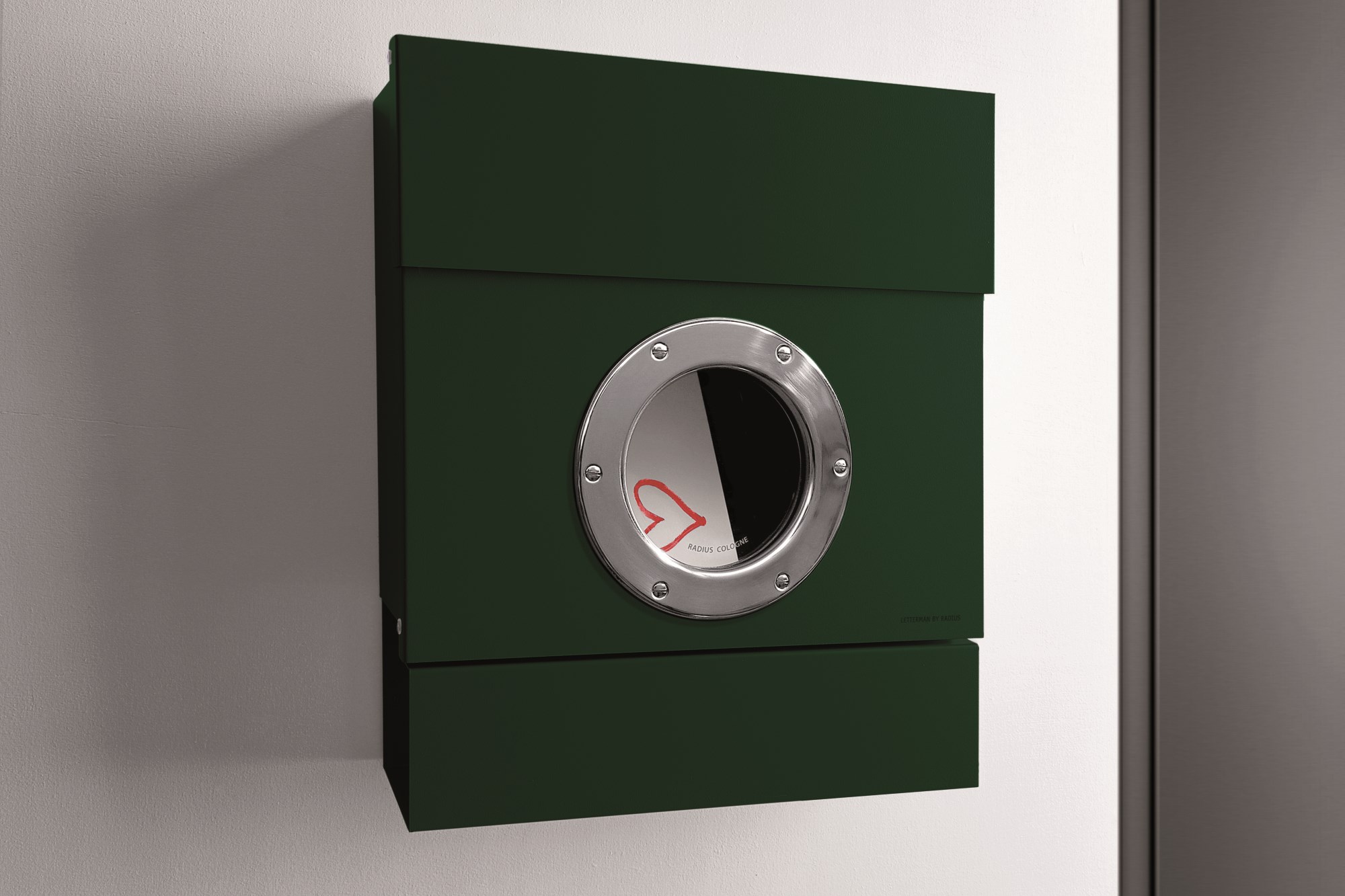 Dunkelgrüner Letterman II Radius Briefkasten mit Bullauge an einer weißen Wand, moderne Hauspostanlage.