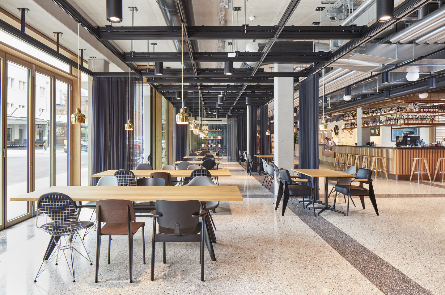 Innenaufnahme eines Restaurants mit Tischen und Stühlen, darunter ein DKR Wire Chair Stuhl von Vitra.