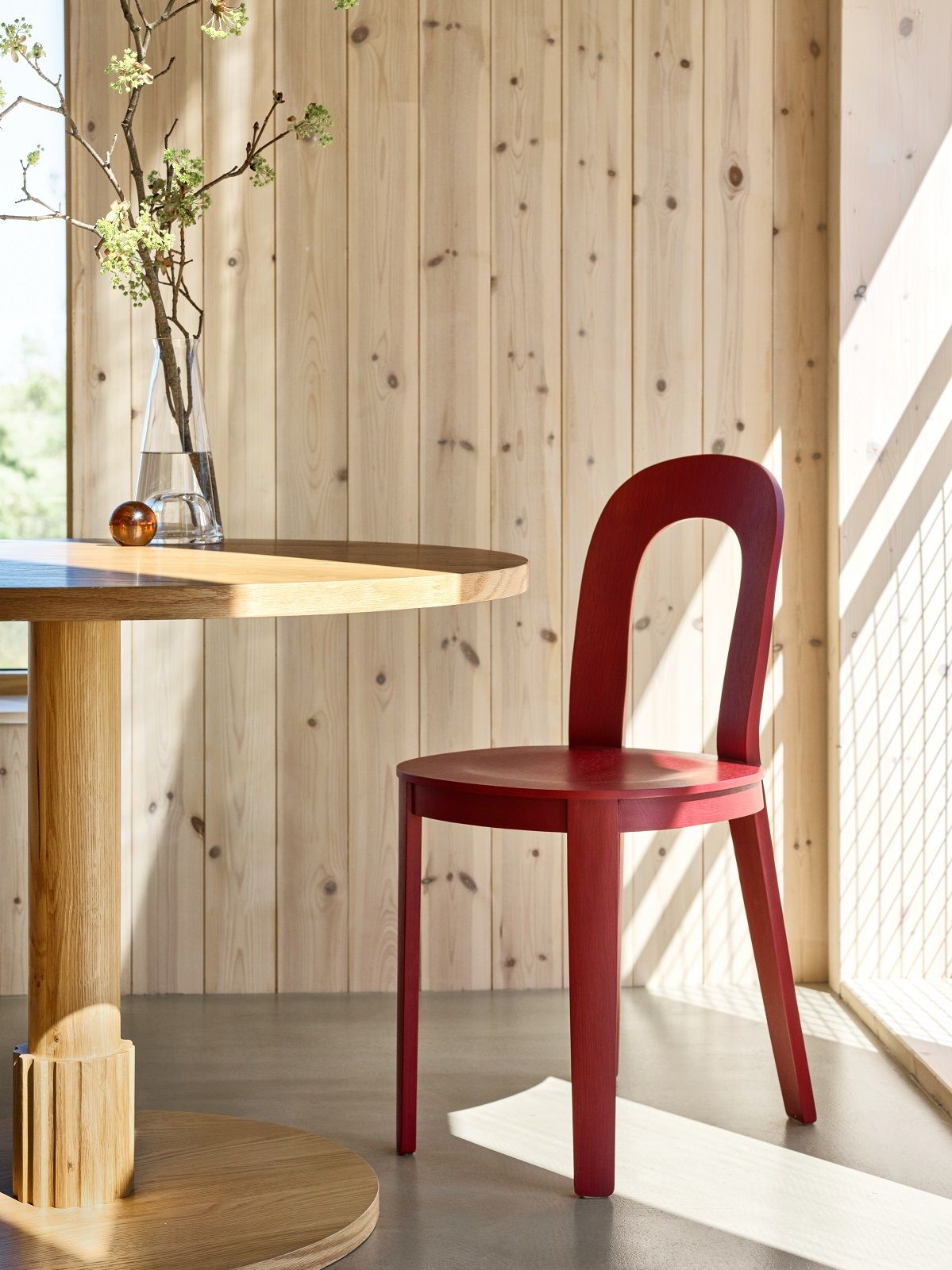 Roter Olivia Chair Holzstuhl von Design House Stockholm neben einem Holztisch in einem hellen Raum.