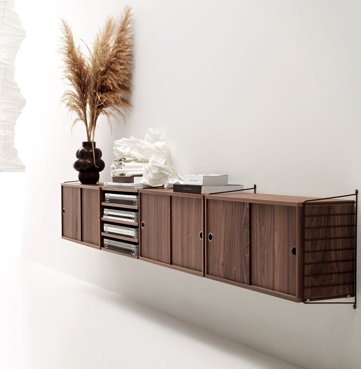 Wandmontiertes Holzregal mit Schiebetüren, dekoriert mit Vase, Pampasgras und Büchern. Modernes Regalsystem für Wohnzimmer.