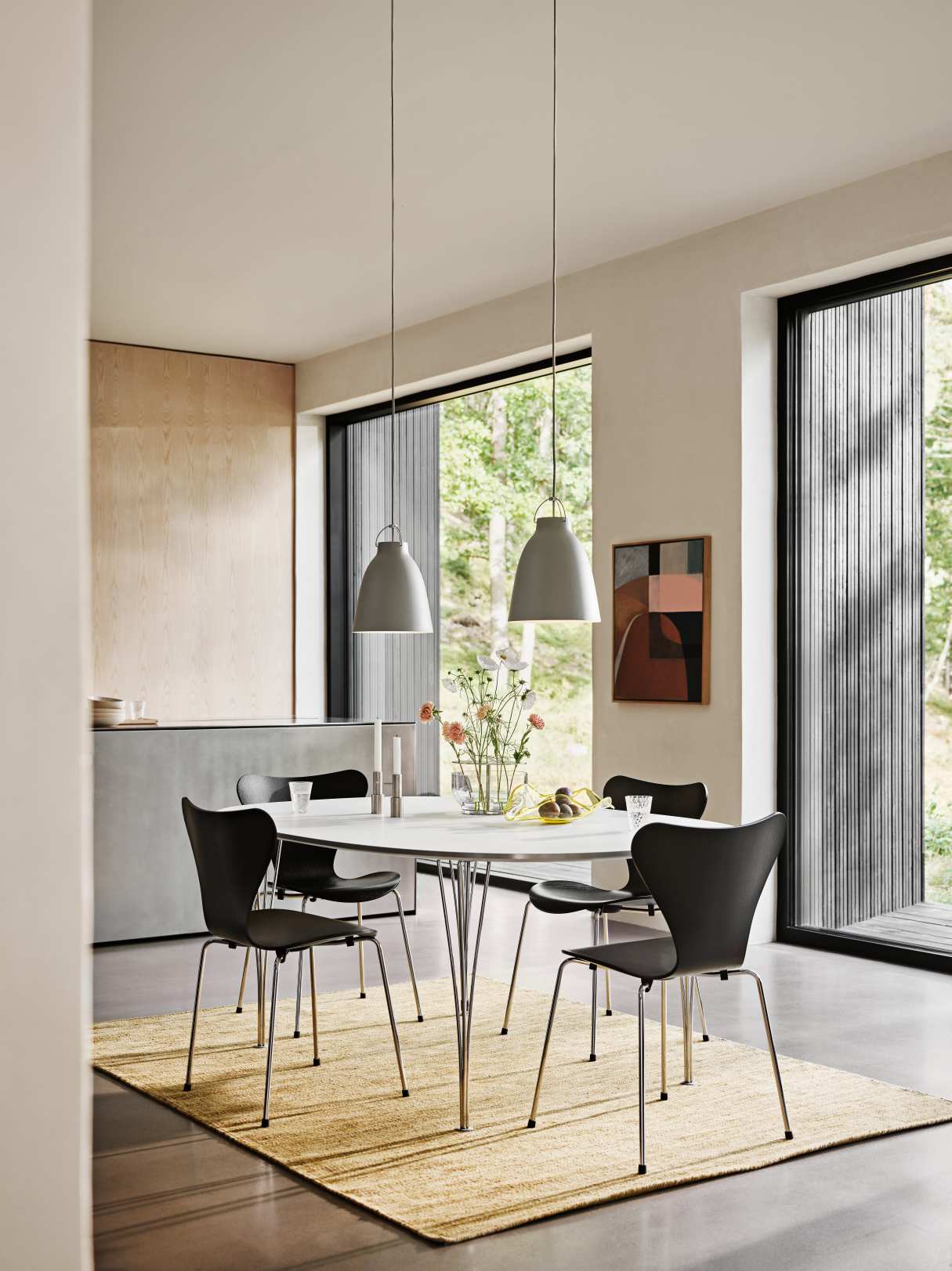 Esszimmer mit zwei grauen Caravaggio Pendelleuchten von Fritz Hansen über einem Esstisch mit Stühlen.