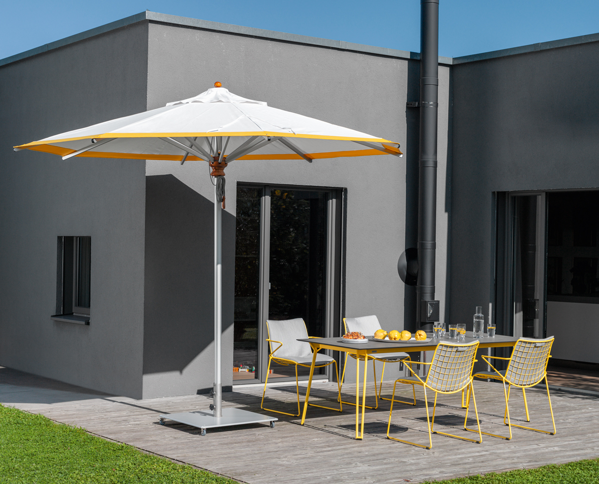 Alusonnenschirm rund grau von Weishäupl spendet Schatten auf einer Terrasse mit Gartenmöbeln.
