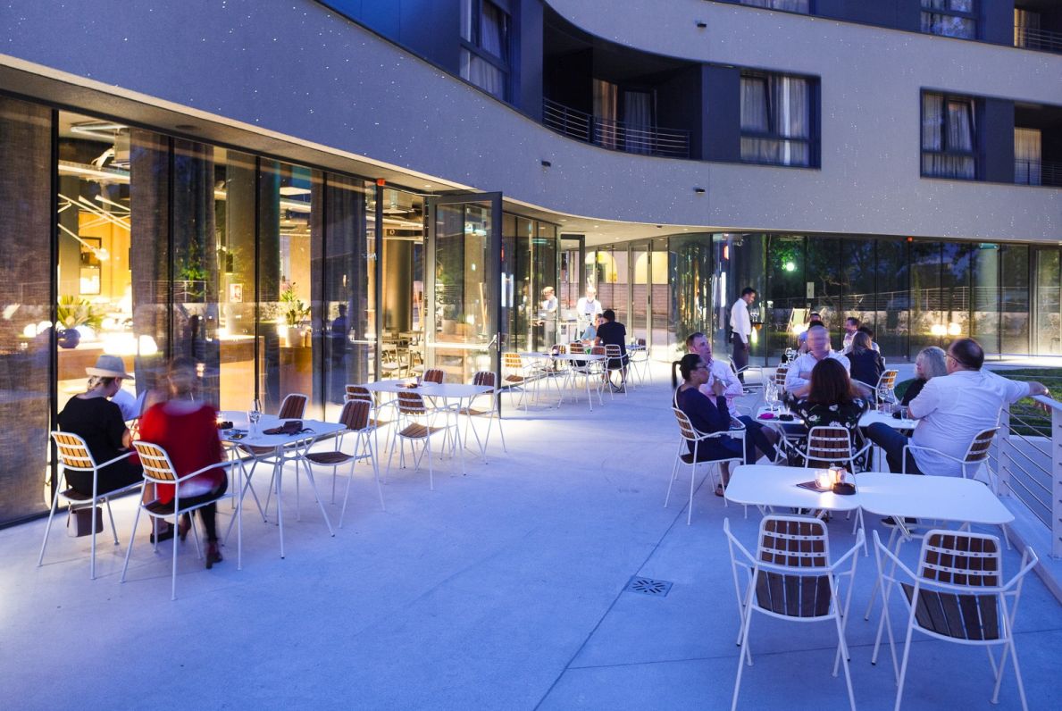 Außenbereich eines Restaurants mit Gästen an Tischen und Osmo Outdoor Stühlen aus Teakholz von Prostoria.