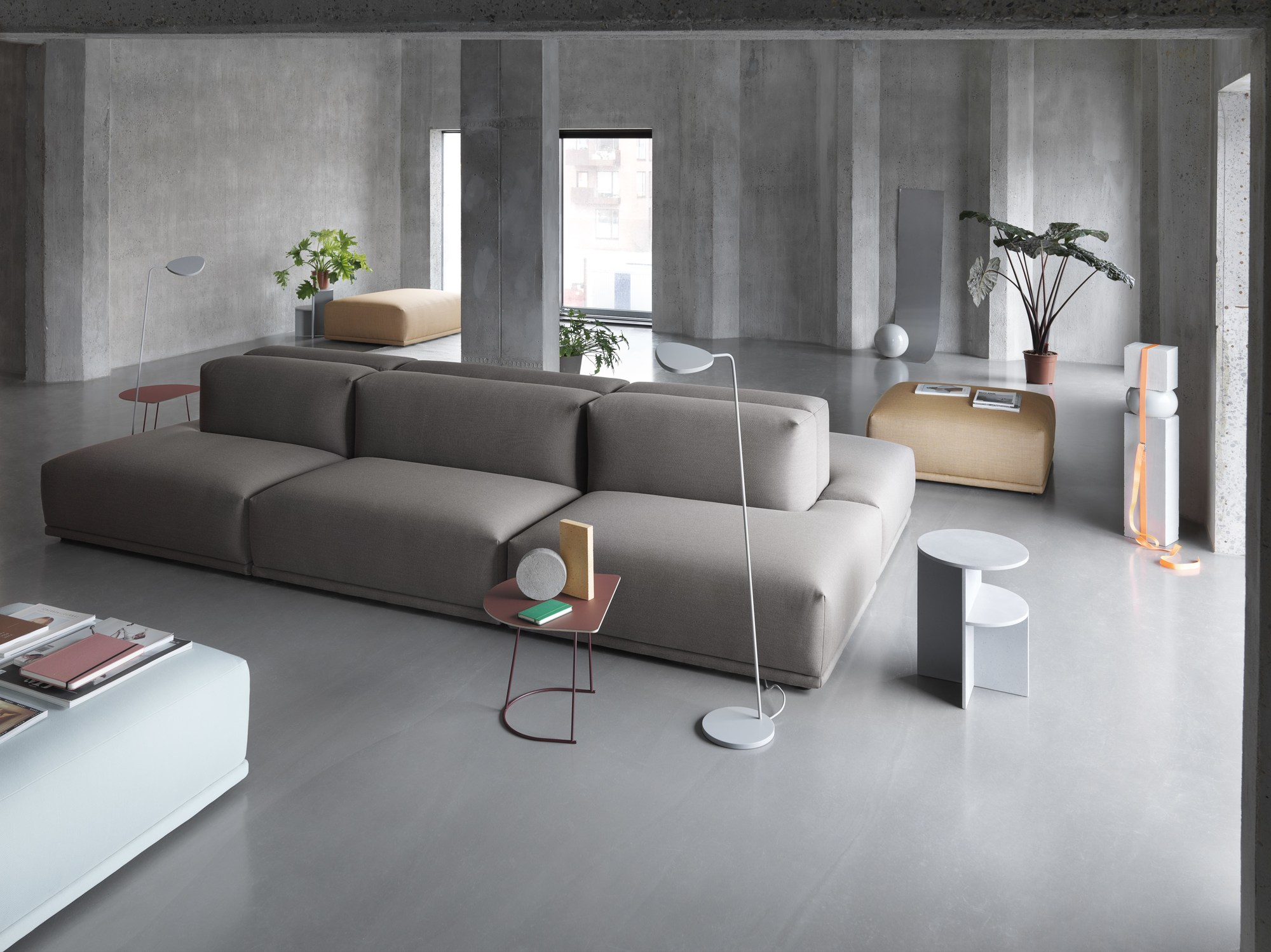 Helle Muuto Leaf Floor Lamp Stehleuchte im modernen Wohnzimmer mit grauem Sofa und Betonwänden.