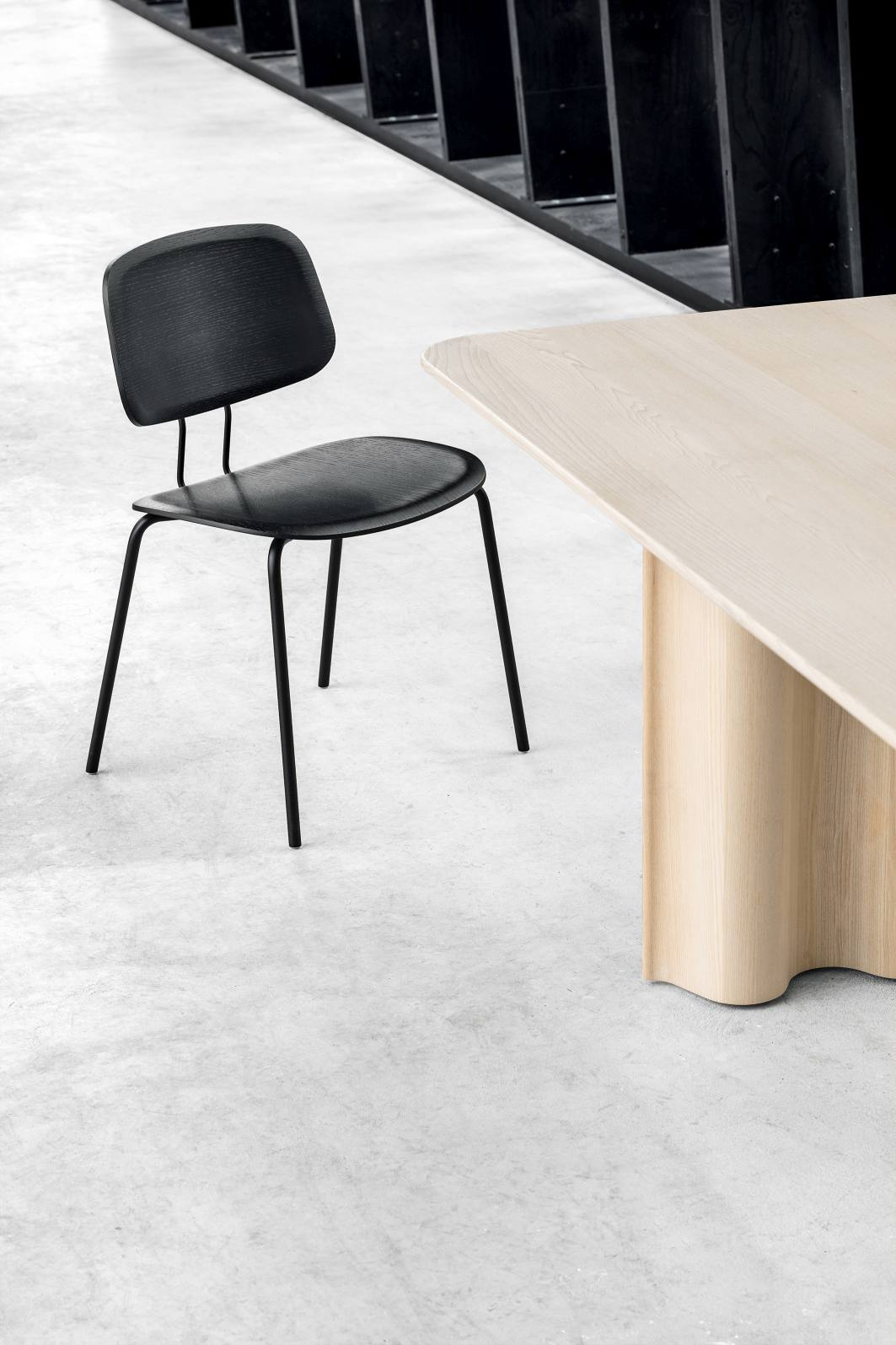Okito Ply Dining Chair Stuhl Zeitraum in Schwarz neben einem hellen Holztisch auf Betonboden.