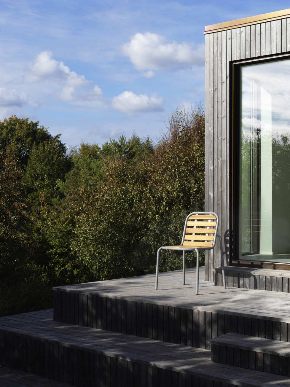 Vig Chair Wood Stuhl von Normann Copenhagen auf Holzterrasse vor modernem Holzhaus.