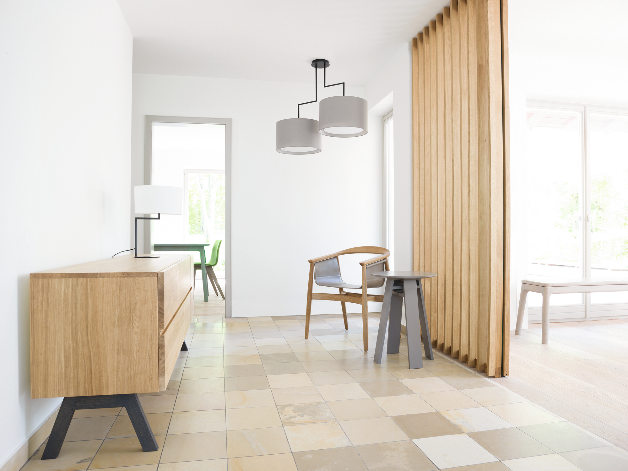 Heller Flur mit Neat Noon Tischleuchte, Sideboard, Stuhl und Holzelement als Raumteiler.