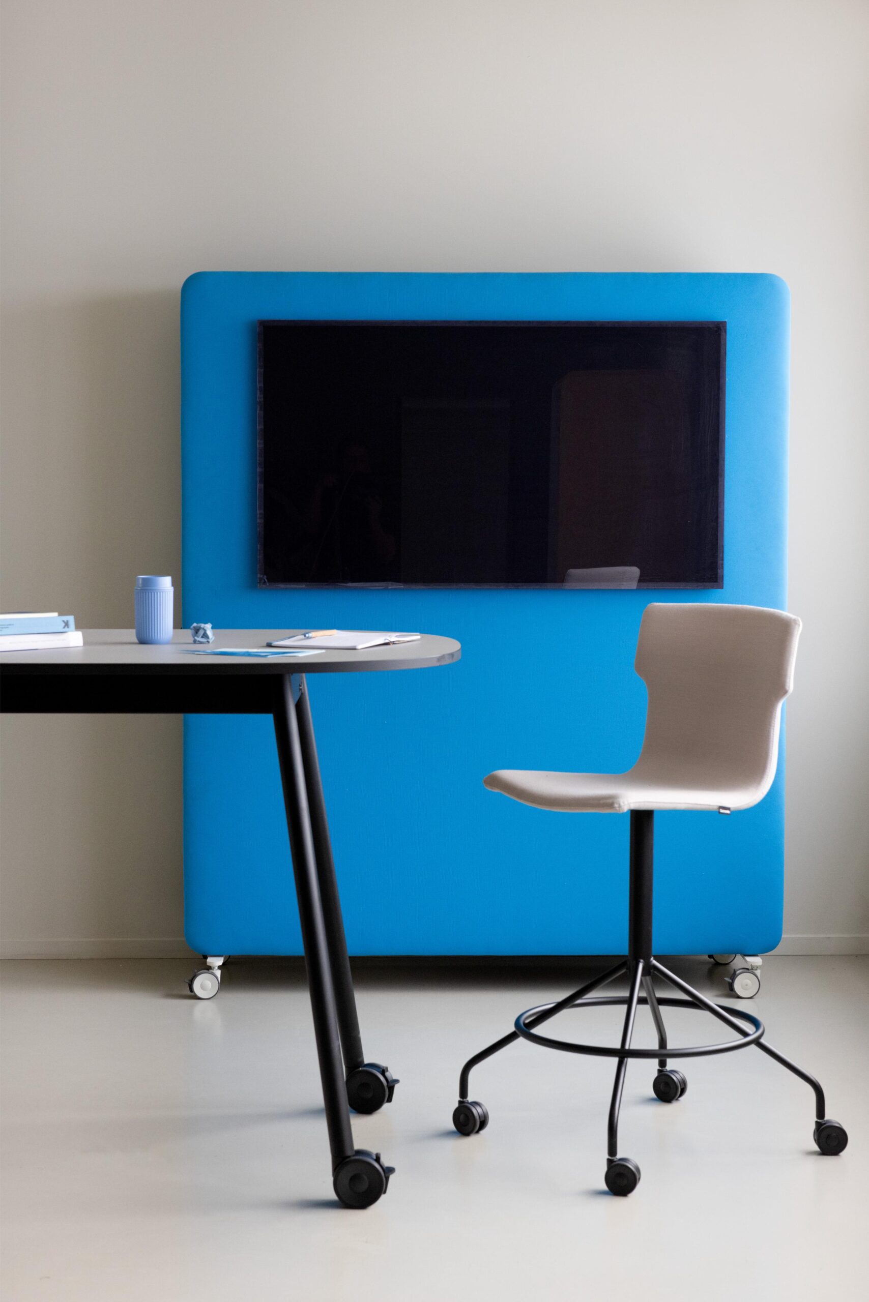Co-Chair Bürodrehstuhl von Cascando, ergonomischer Hocker mit Rollen vor blauer Akustikwand mit Bildschirm.