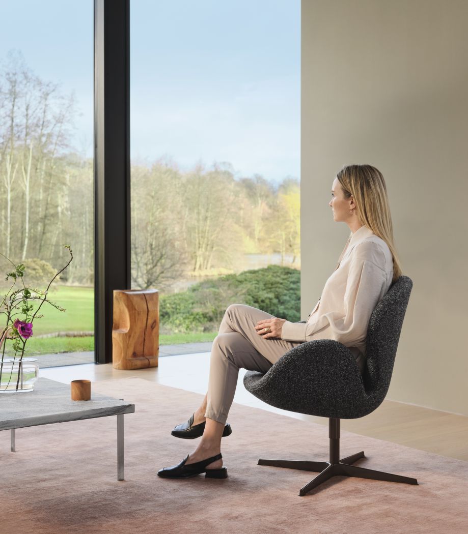 Frau sitzt entspannt im grauen Swan Sessel von Fritz Hansen. Designmöbel für Wohnzimmer.