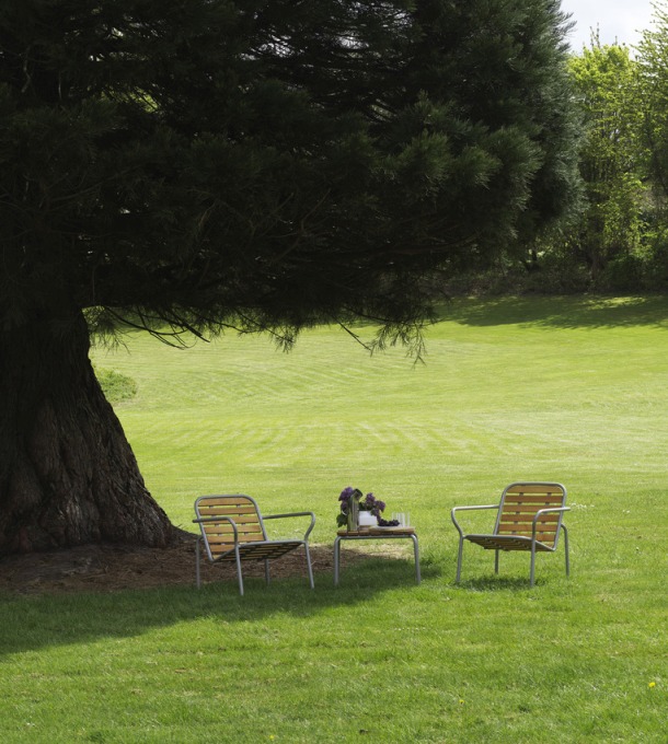 Normann Copenhagen Vig Table Outdoor mit zwei Stühlen auf einer grünen Wiese unter einem Baum.