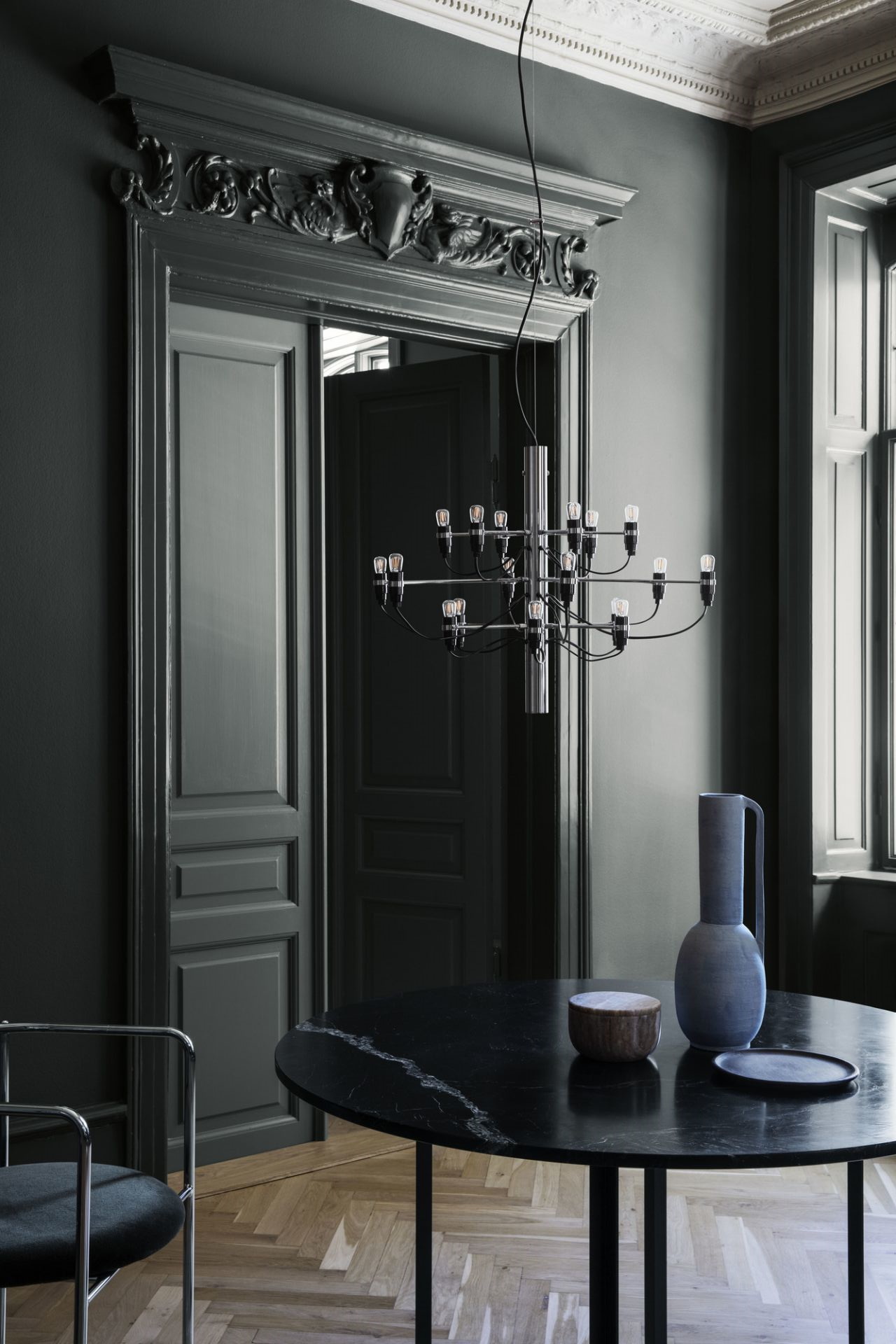 Moderne schwarze Kronleuchter-Pendelleuchte über rundem Marmortisch in elegantem, dunklem Esszimmer. Design Lampe für stilvolle Innenarchitektur.