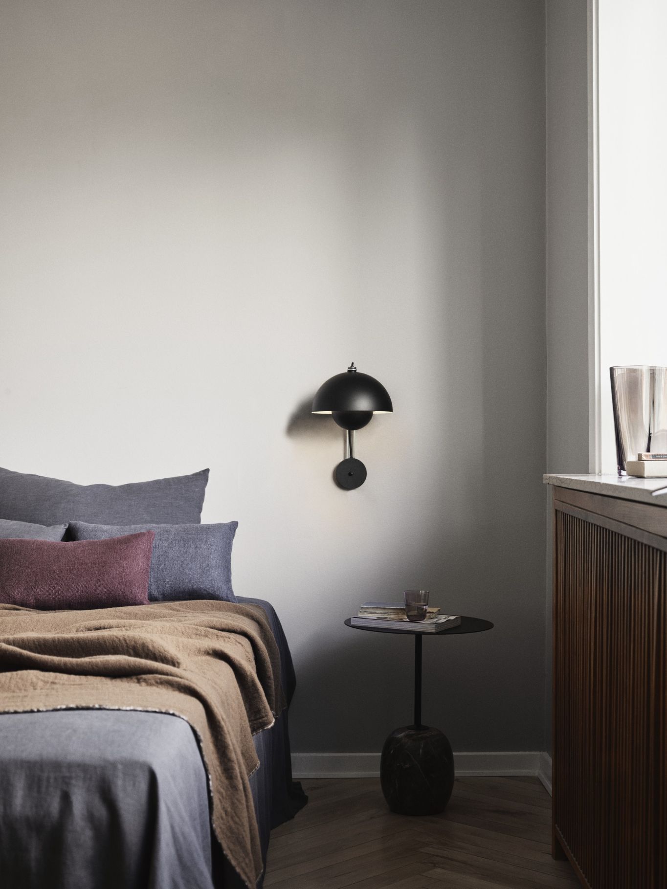 Nahaufnahme einer schwarzen Flowerpot VP8 Wandleuchte von AndTradition neben einem Bett in einem Schlafzimmer.