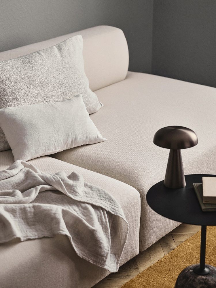 AndTradition Como SC53 Akku Tischleuchte auf schwarzem Beistelltisch neben beigem Sofa.
