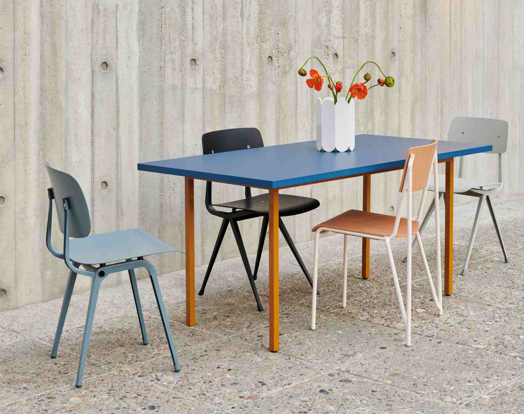 Hay Two Colour Table Esstisch 240 cm hellgrau-ocker mit vier Stühlen und Blumenvase vor Betonwand.