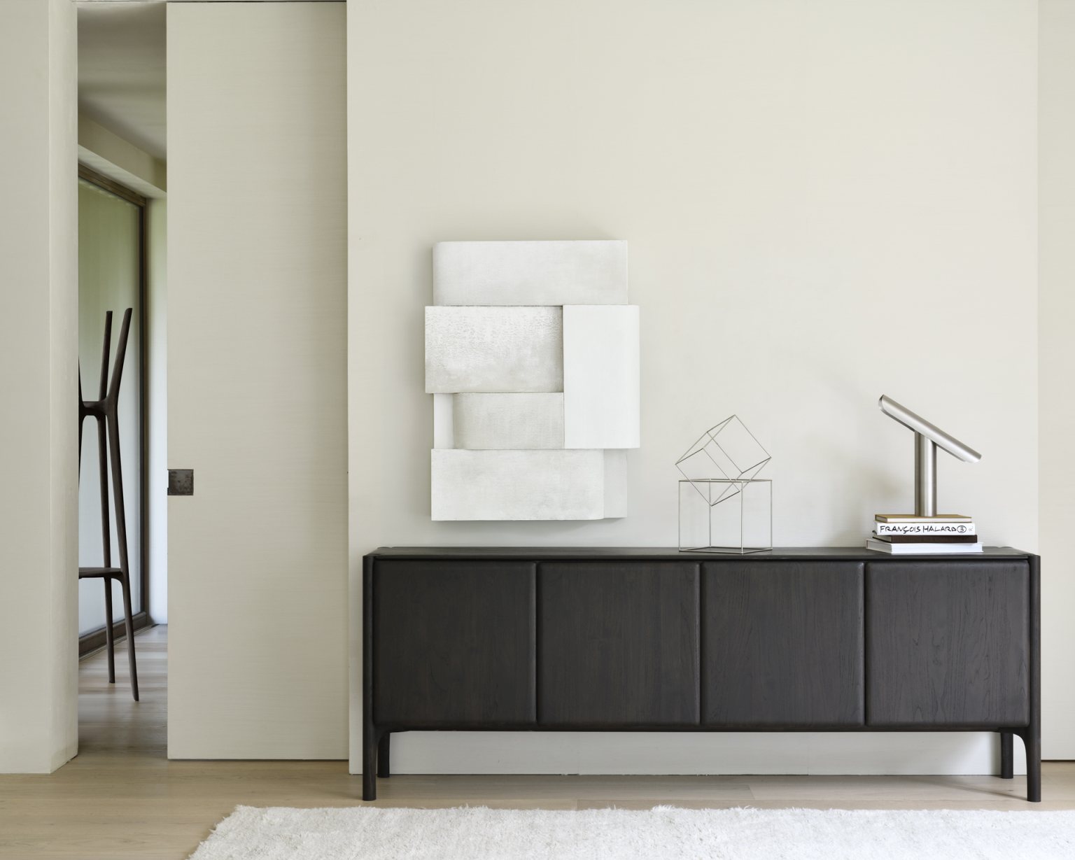 Ethnicraft Sideboard aus dunklem Holz mit minimalistischer Dekoration und weißem Teppich im modernen Wohnzimmer.