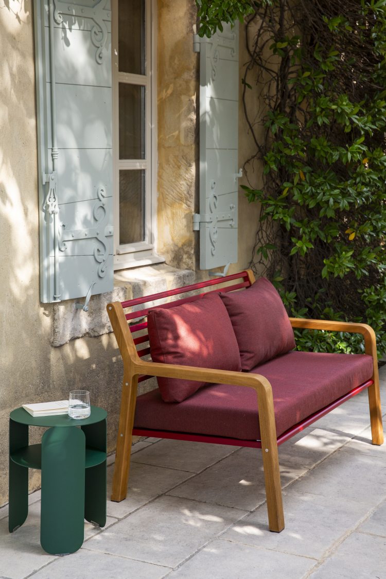 Nahaufnahme des Fermob Somerset 2-Sitzer Outdoor Sofas in Rot mit Holzelementen und grünen Beistelltisch.