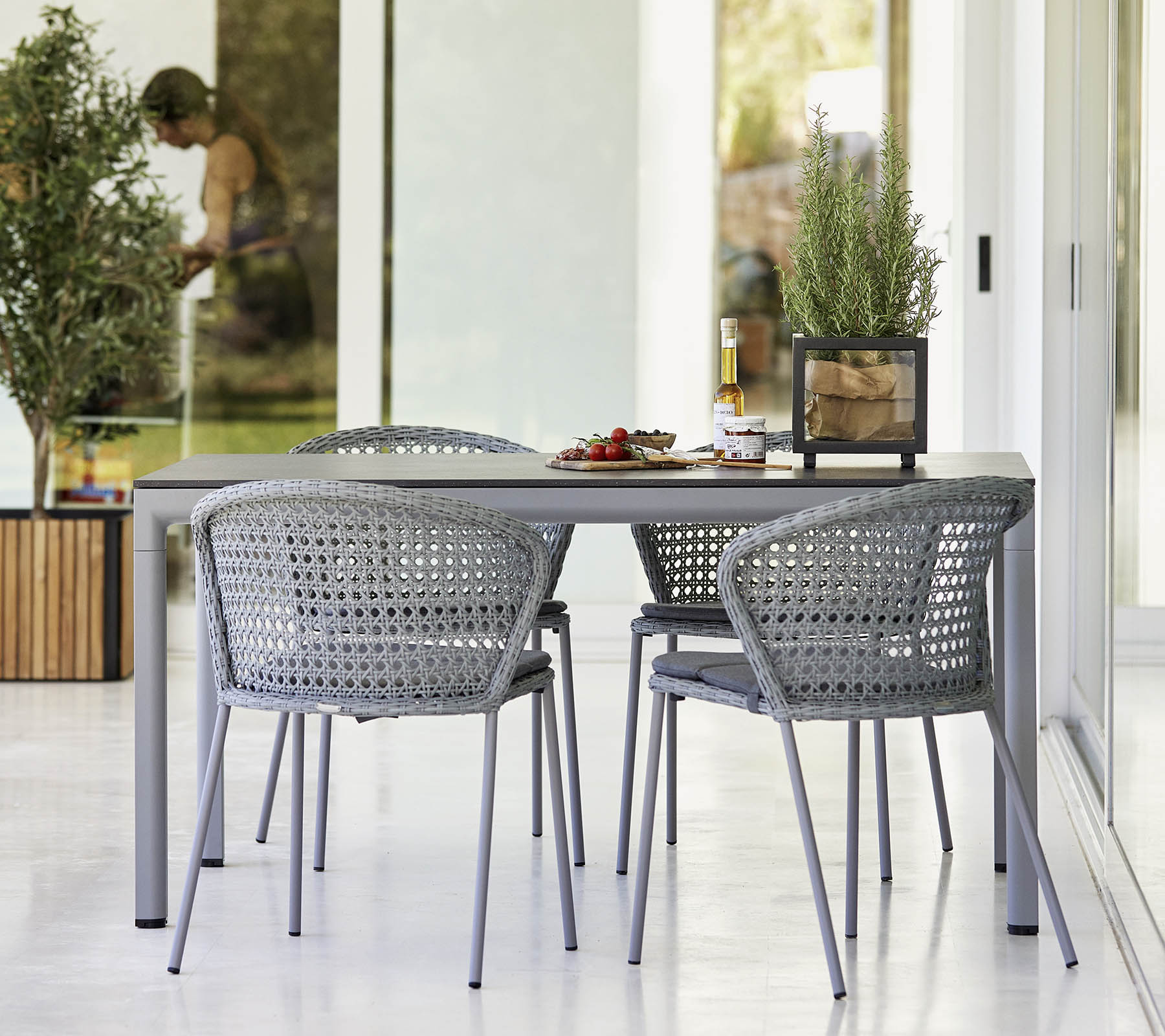 Graue Cane-Line Lean Stühle mit Rattan-Geflecht an Esstisch im Außenbereich. Gartenmöbel für Terrasse.