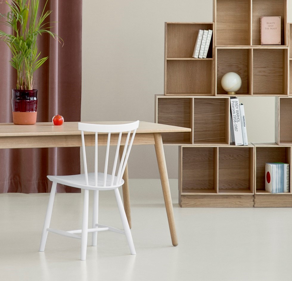 Heller Esstisch aus Holz mit weißem Stuhl und modularem Holzregal im Hintergrund.