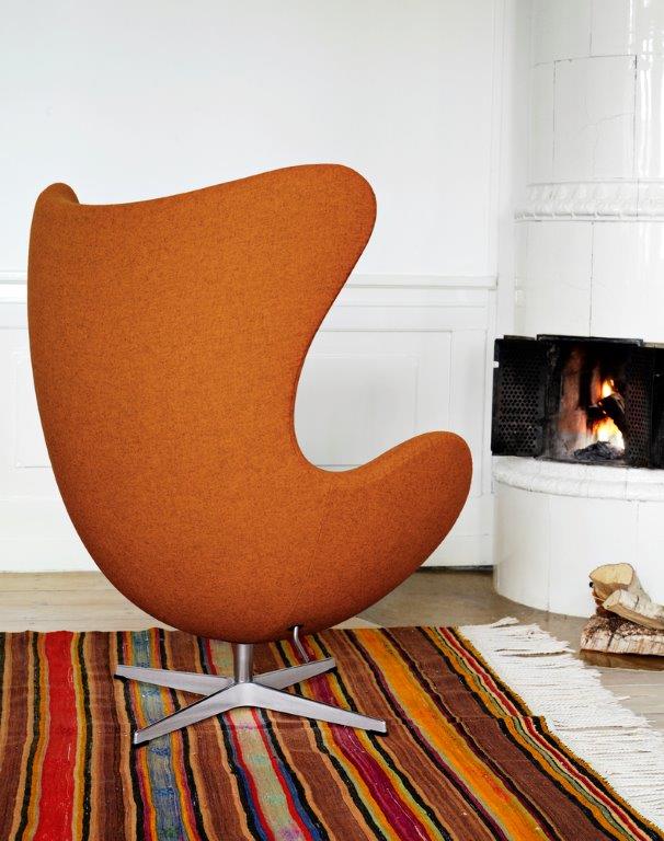 Orangefarbener Egg Chair Sessel von Fritz Hansen mit Hocker auf einem bunten Teppich vor Kamin.