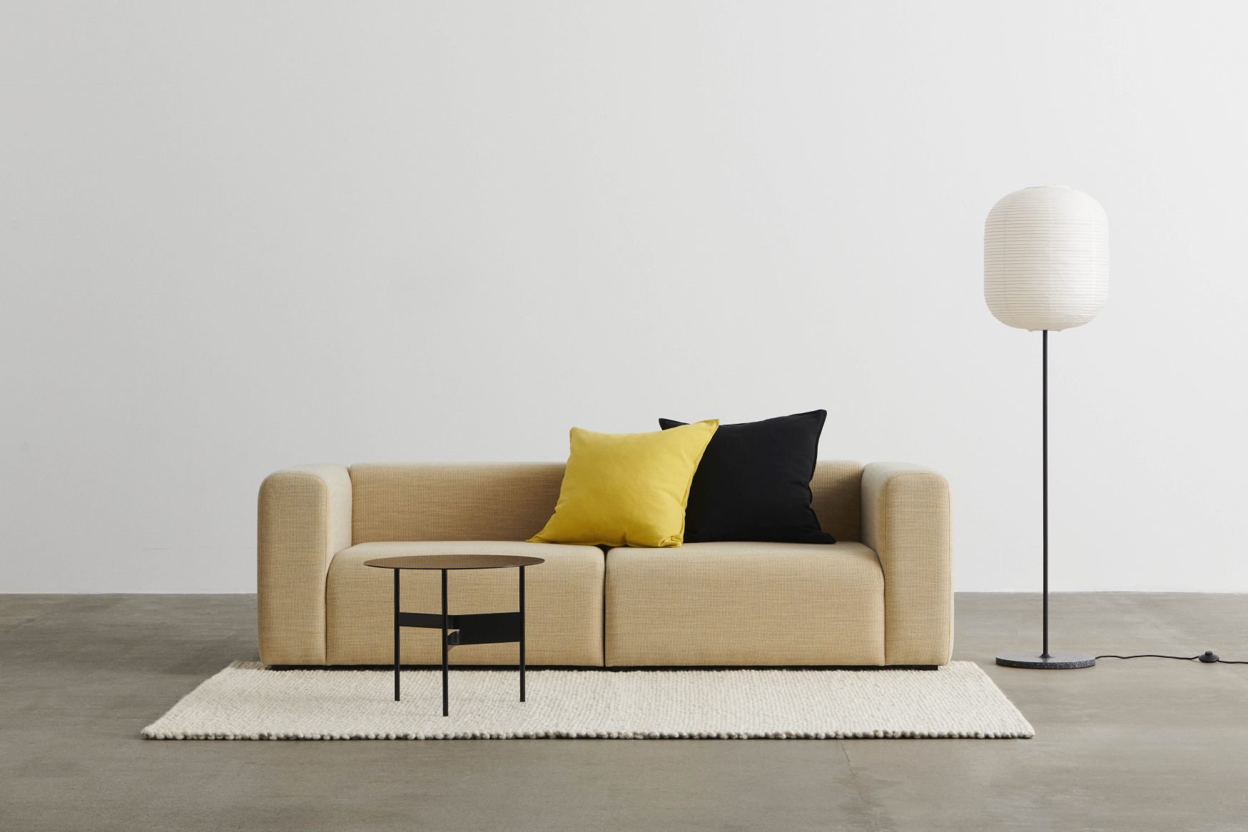 Beiges Mags Sofa mit gelbem und schwarzem Kissen, kleinem Tisch und Stehlampe.