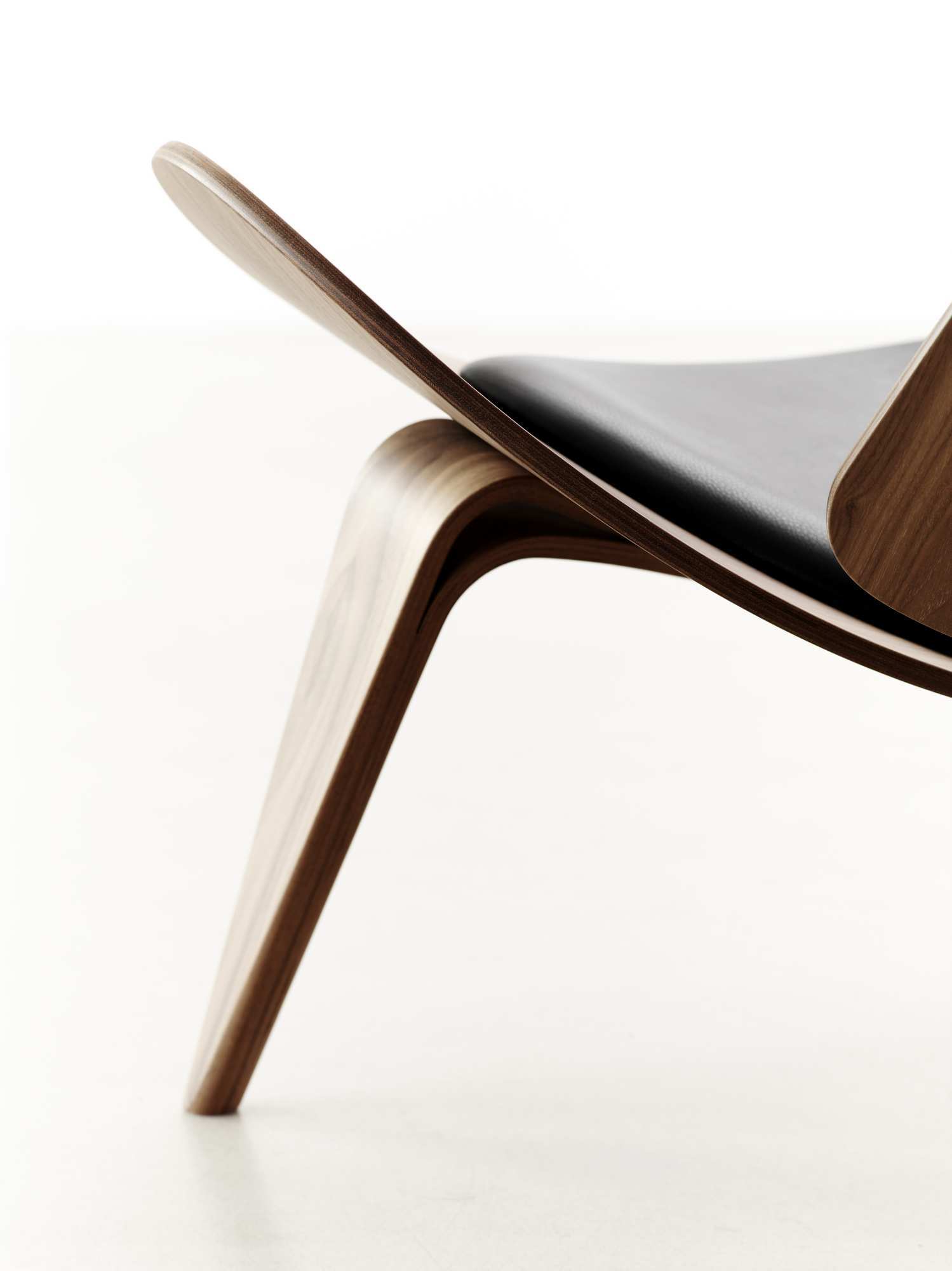 Detailaufnahme des CH07 Shell Chair Stuhls von Carl Hansen mit schwarzem Lederbezug und Holzgestell.
