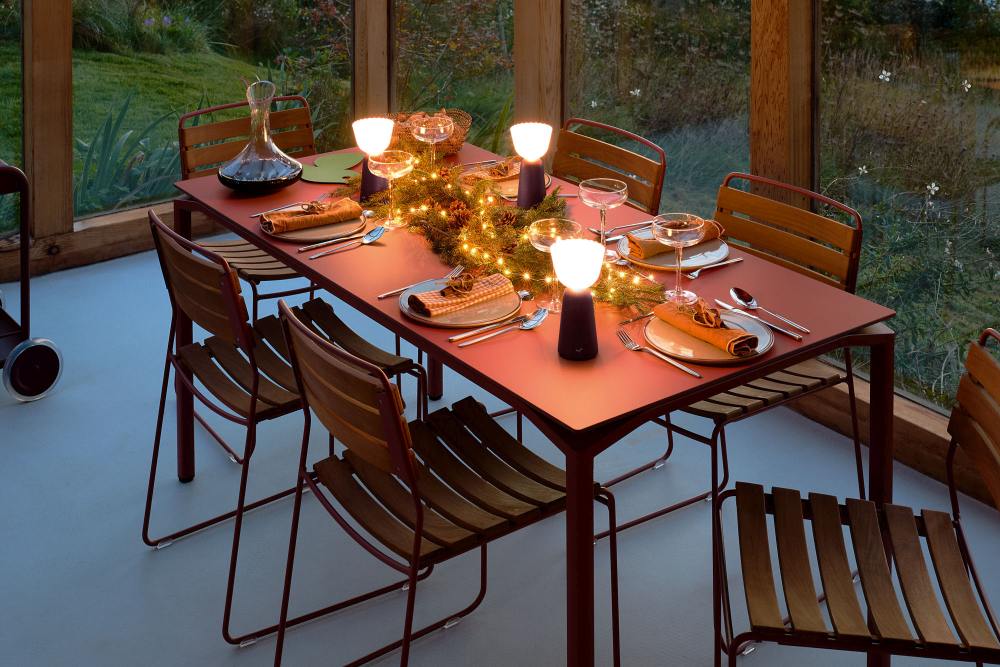 Esstisch mit Teakholzstühlen und festlicher Dekoration, inklusive Lampen, Geschirr und Getränken. Outdoor-Möbel für Garten und Terrasse.