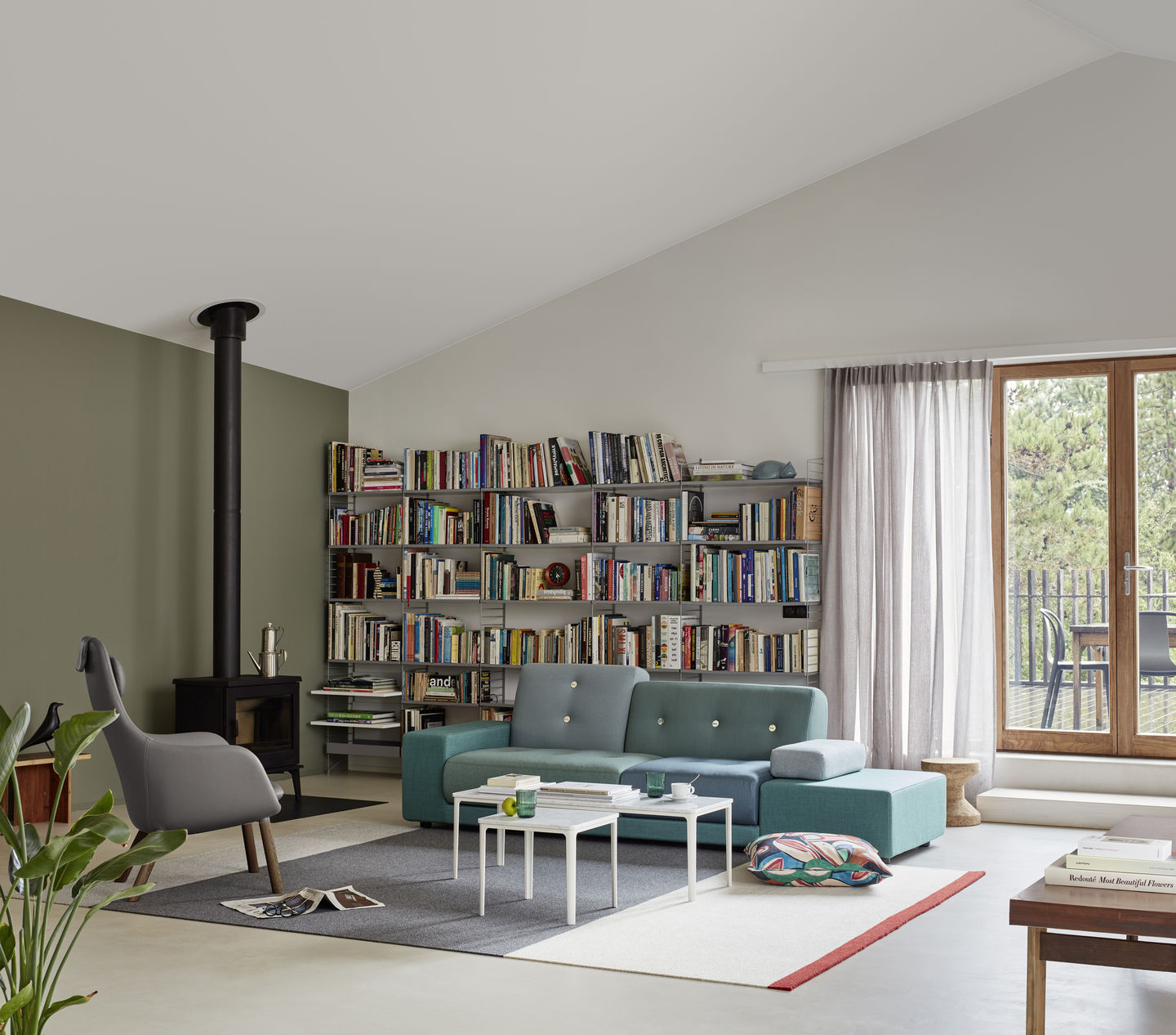 Wohnzimmer mit blauem Polder Sofa von Vitra, Bücherregal und Kaminofen.