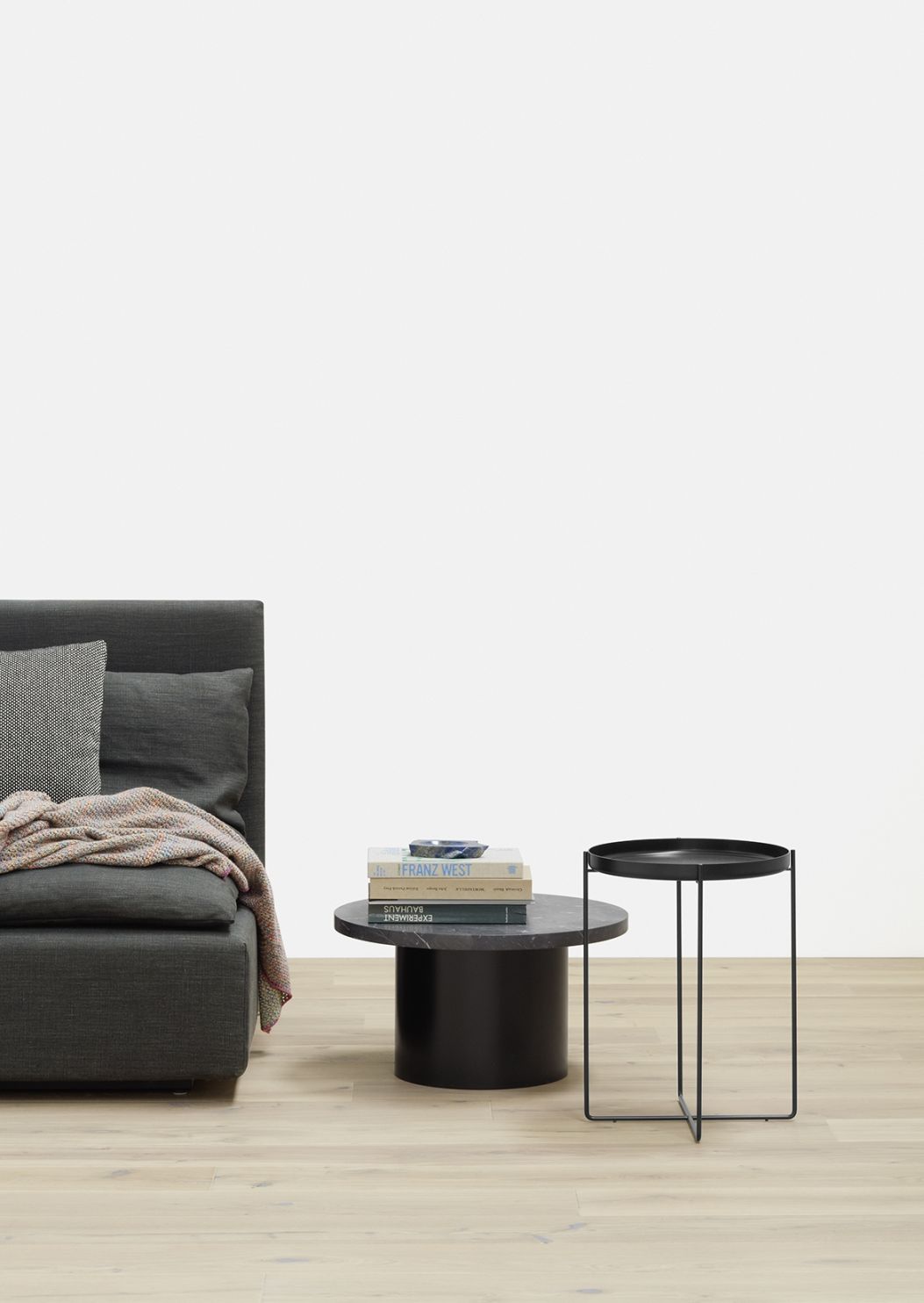 Enoki Beistelltisch von e15: Schwarzer Marmortisch und filigraner Metalltisch neben einem grauen Sofa.