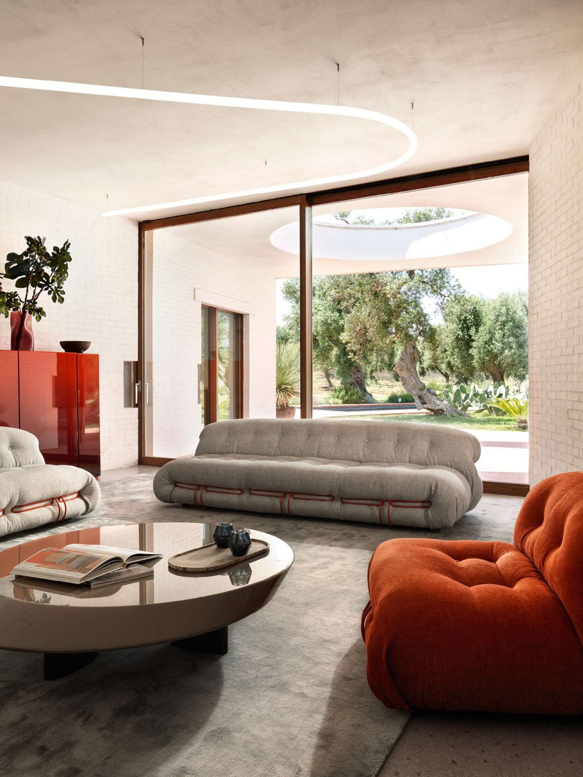 Wohnzimmer mit grauer Modulsofa, orangefarbenem Sessel und rundem Couchtisch. Modernes Möbeldesign für stilvolles Wohnen.