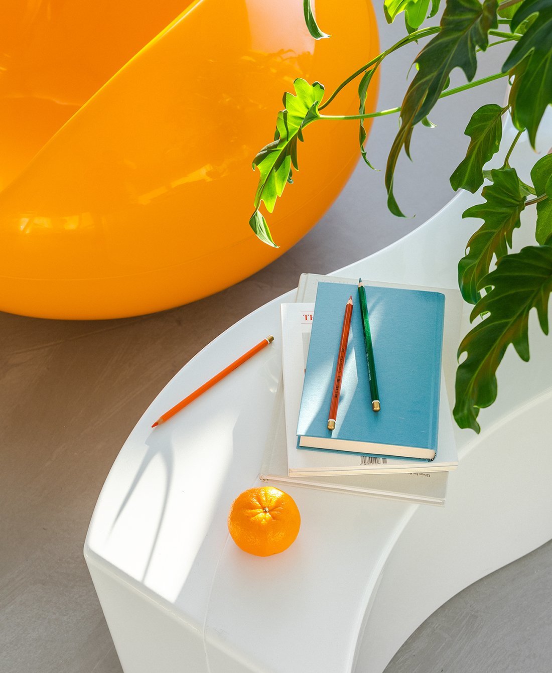Detailaufnahme: Blauer Pastil Stuhl, Designklassiker, mit Büchern, Stiften und Orange dekoriert. Sitzmöbel für Wohnraum.