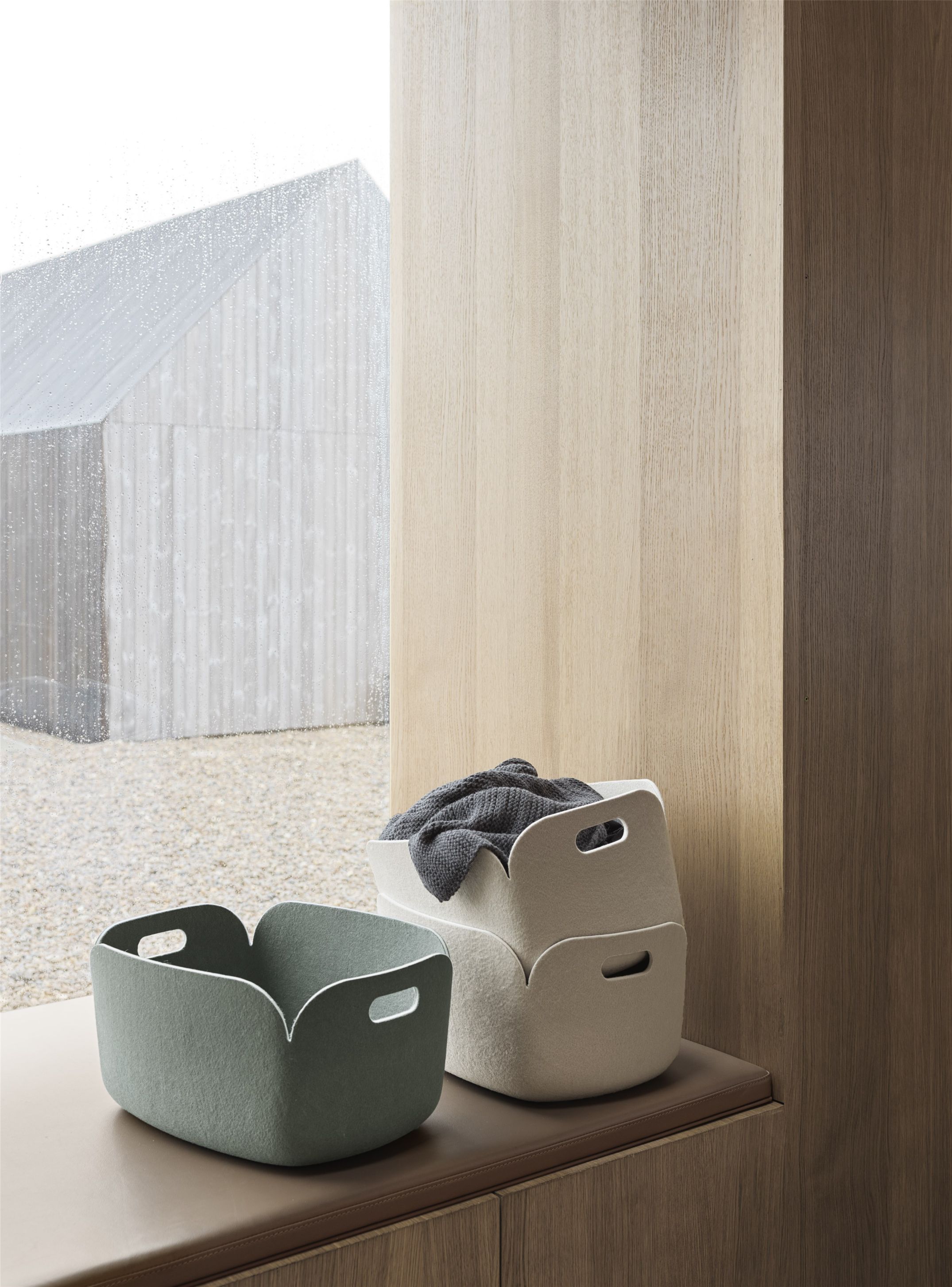 Zwei Muuto Restore Aufbewahrungskörbe: Staubgrün und Beige, einer mit Decke, auf Fensterbank.