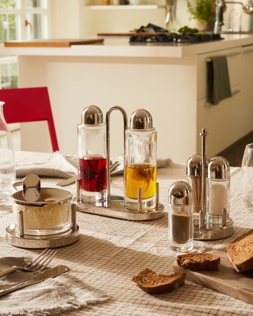 Alessi Käsedose 5071 und Gewürzständer-Set aus Edelstahl auf einem gedeckten Tisch, ideal für Küche und Esstisch.