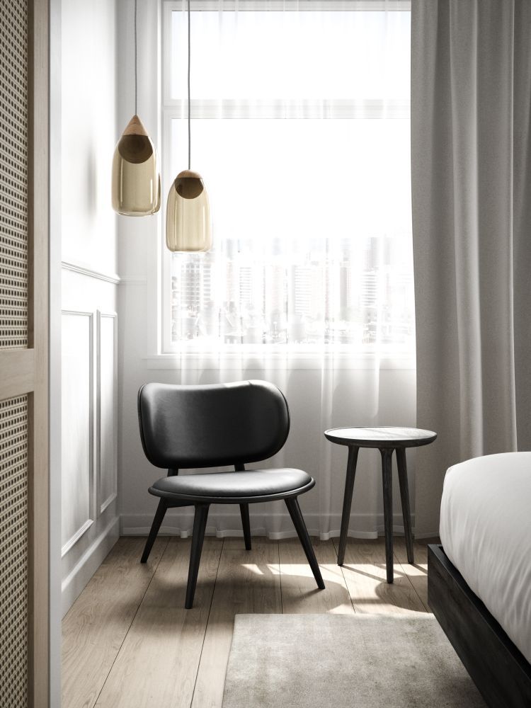 Schwarzer Design-Stuhl mit kleinem Beistelltisch und Pendelleuchten in hellem Schlafzimmer mit Holzboden und großem Fenster.