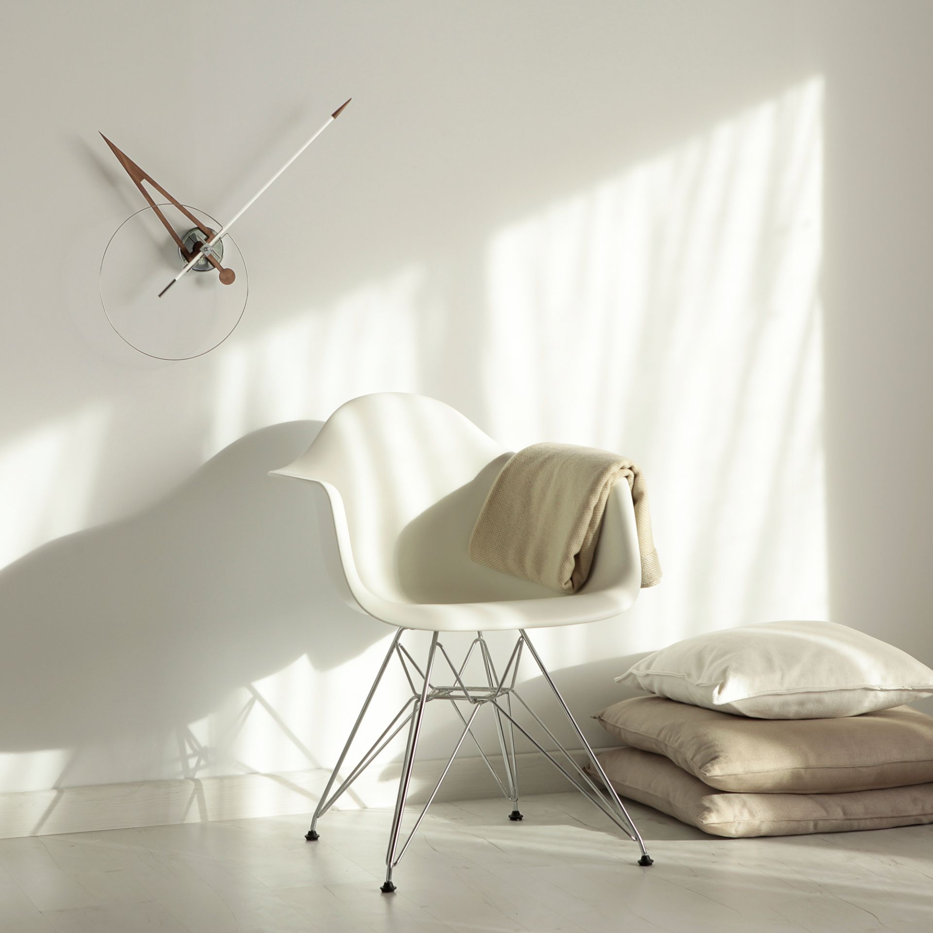 Heller Wohnraum mit Design-Stuhl, Decke, Kissen und moderner Wanduhr für stilvolles Interieur.