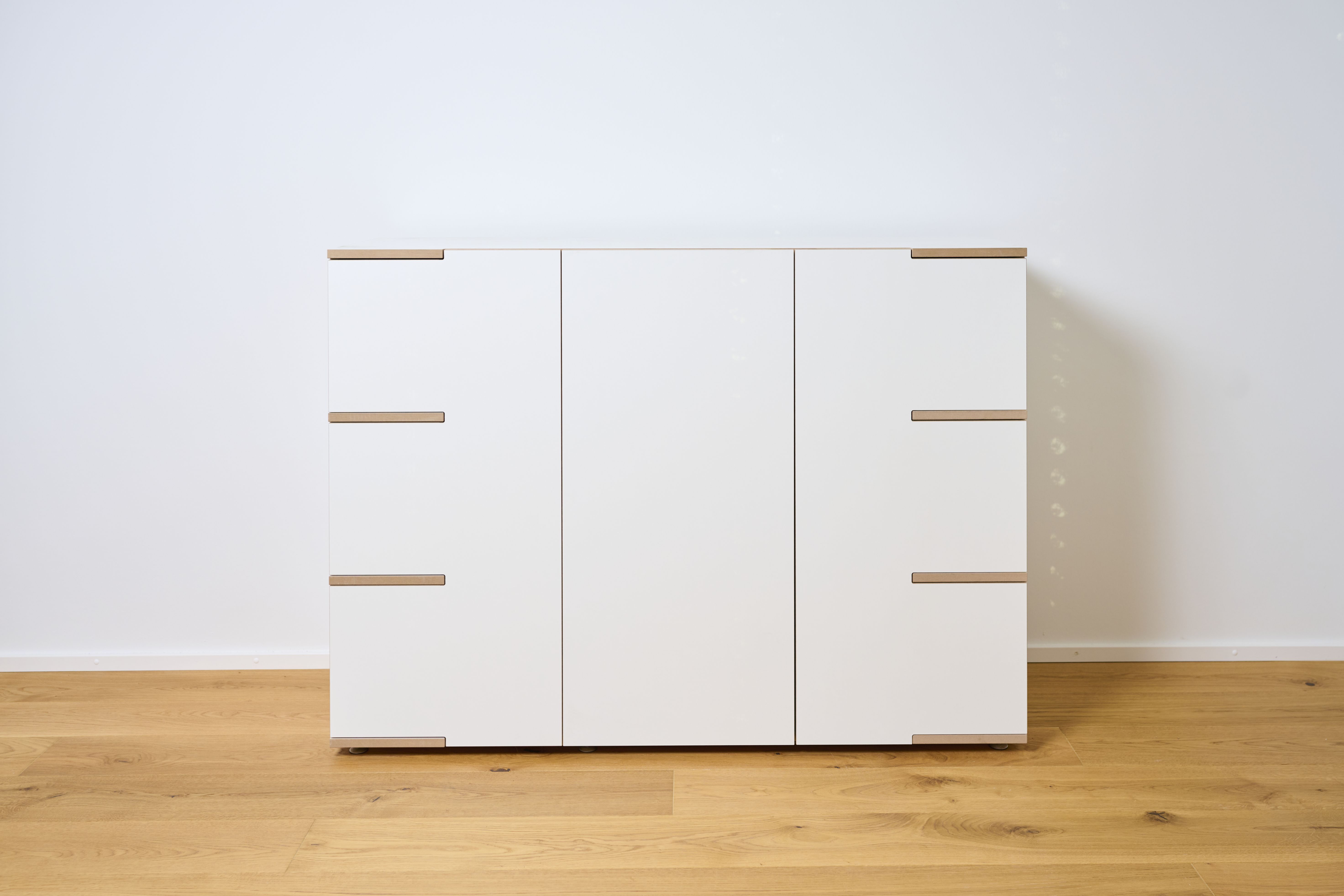 Tojo Stau Sideboard aus weißem Holz mit drei Türen und Griffen auf hellem Holzboden.