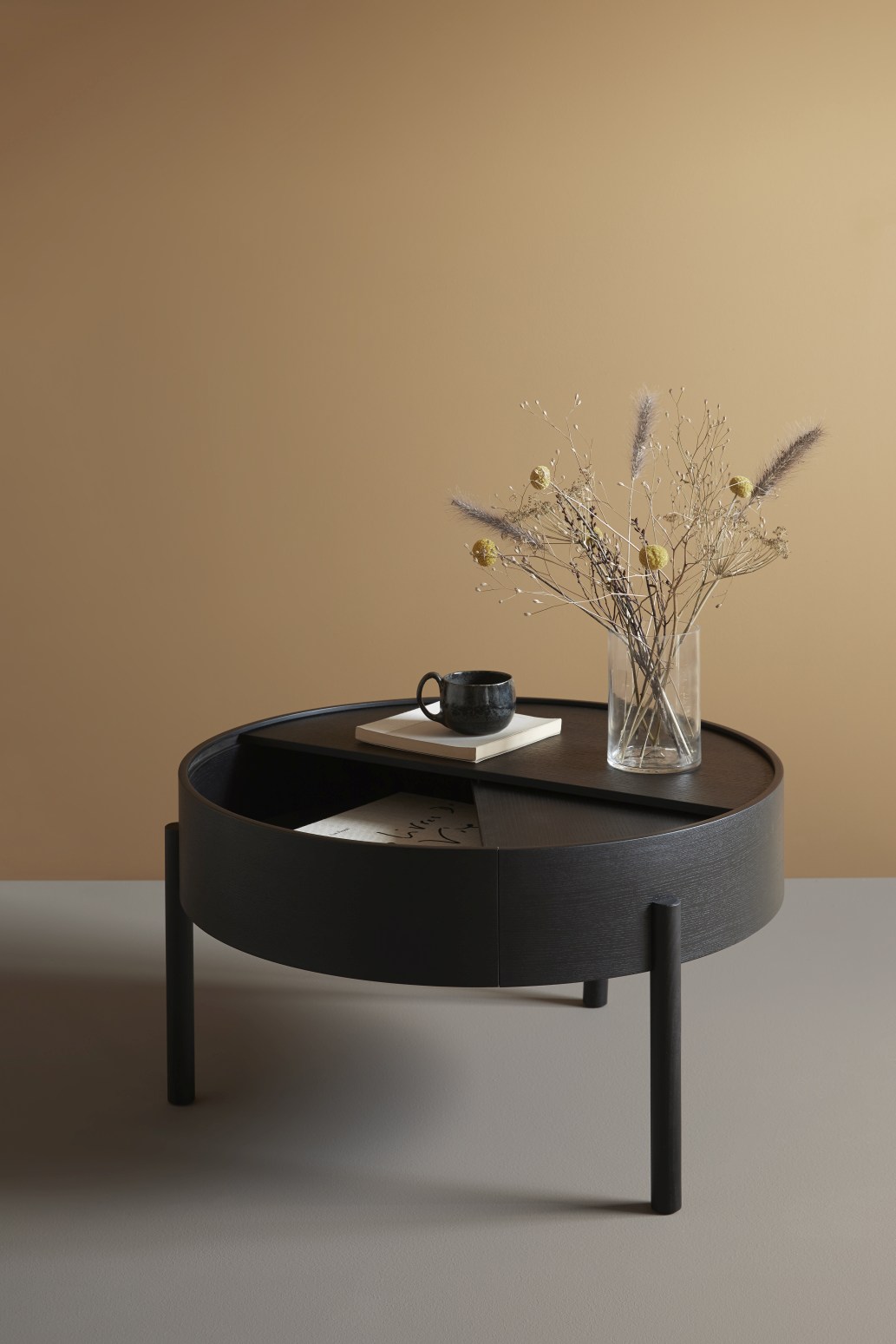 Schwarzer Arc Couchtisch von Woud, runder Beistelltisch mit Stauraum, Kaffeetasse und Dekoration.