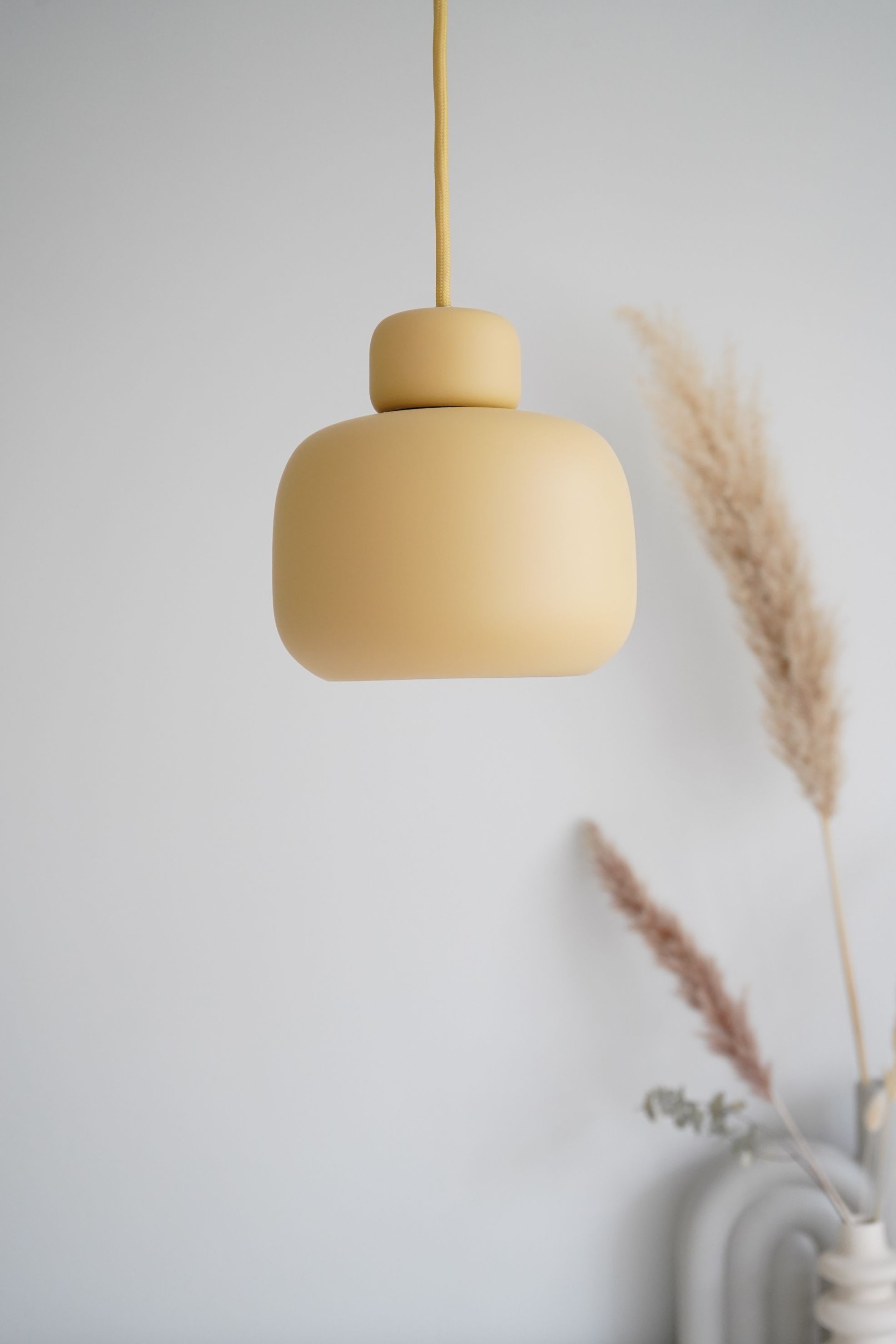 Nahaufnahme der kleinen Woud Stone Pendant Pendelleuchte in Gelb mit Textilkabel vor weißer Wand.