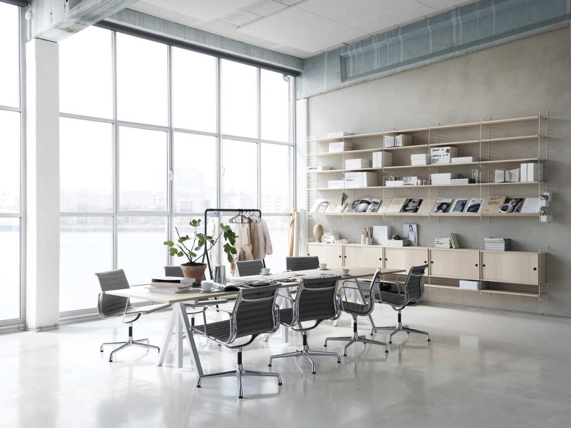 Wordesk Table Schreibtisch von String Furniture in einem hellen Konferenzraum mit Regalsystem und Bürostühlen.